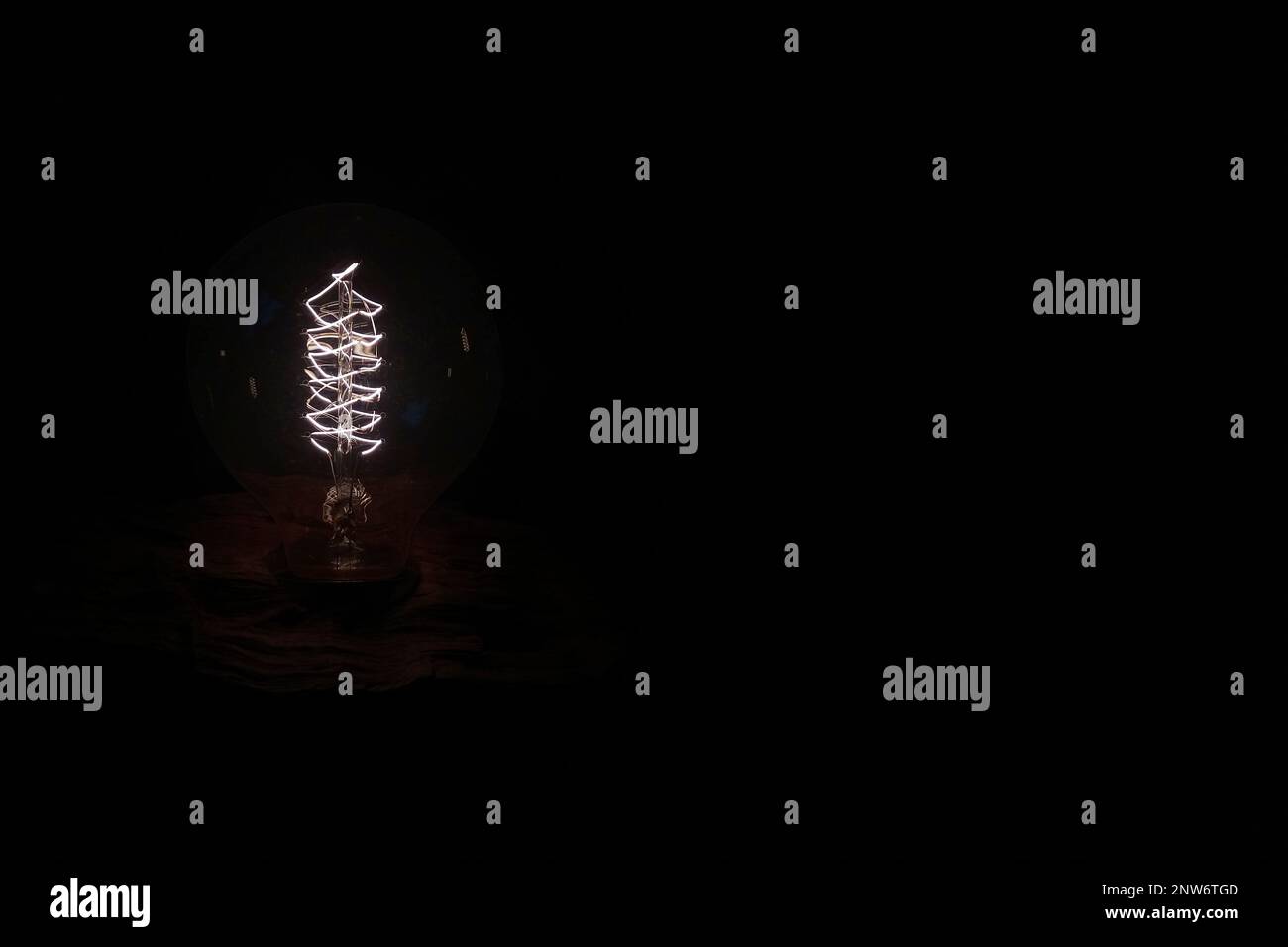 Nahaufnahme einer Glühlampe im Retro-Stil, die auf ein Holzstück geschraubt wurde, isoliert auf schwarzem Hintergrund. Stockfoto