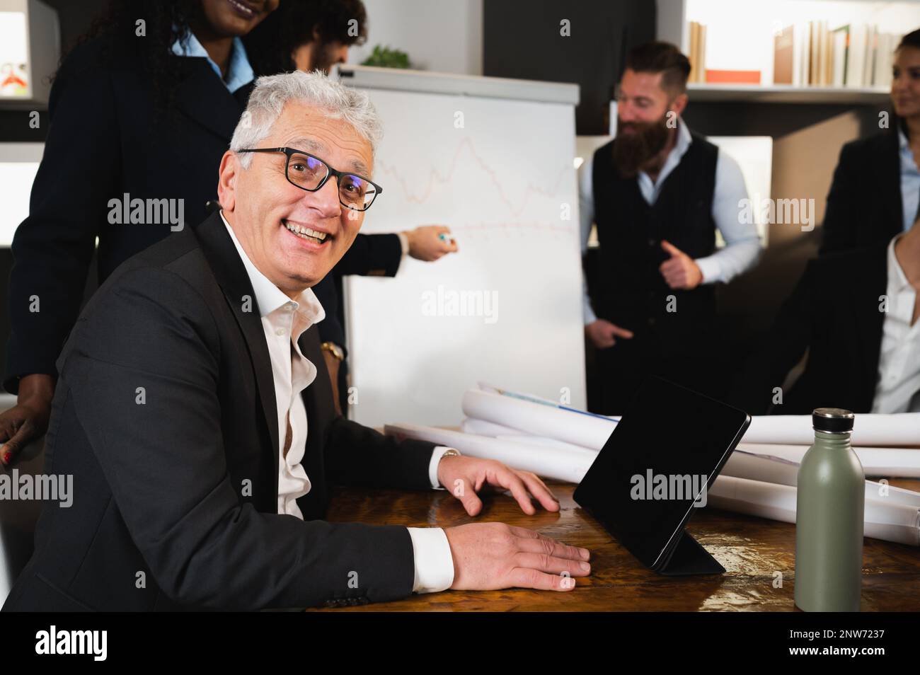 Seitenporträt eines leitenden Geschäftsmanns, der vor der Kamera lächelt. Leute, die in Vorstandssitzungen arbeiten. Stockfoto