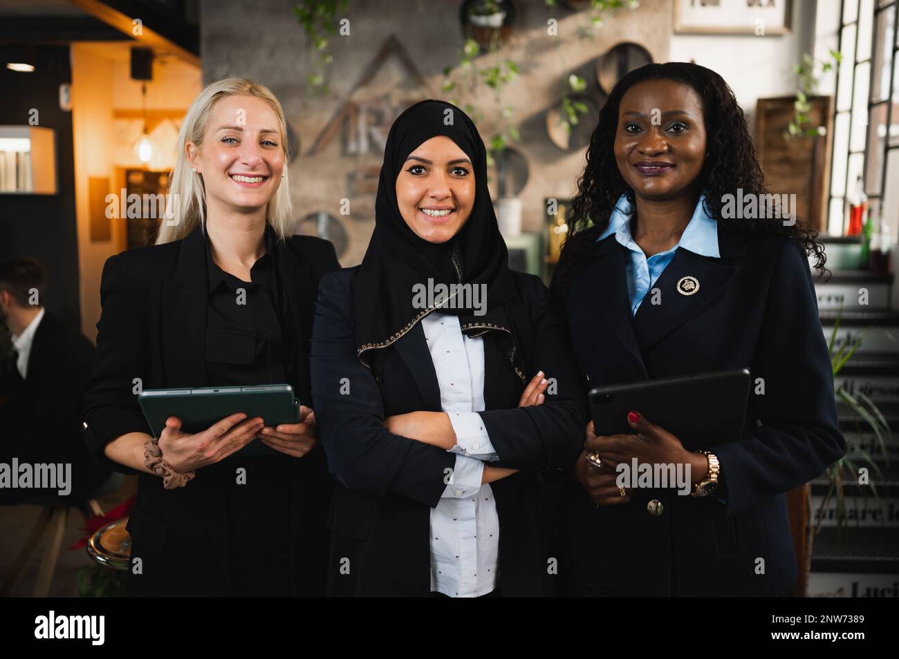 Drei junge, elegante Geschäftsfrauen mit unterschiedlicher ethnischer Herkunft, die vor der Kamera stehen und lächeln. Stockfoto