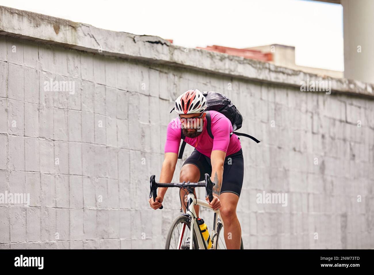 Ein Radfahrer mit Brille und Helm fährt durch die Stadt vor dem Hintergrund einer Betonwand Stockfoto