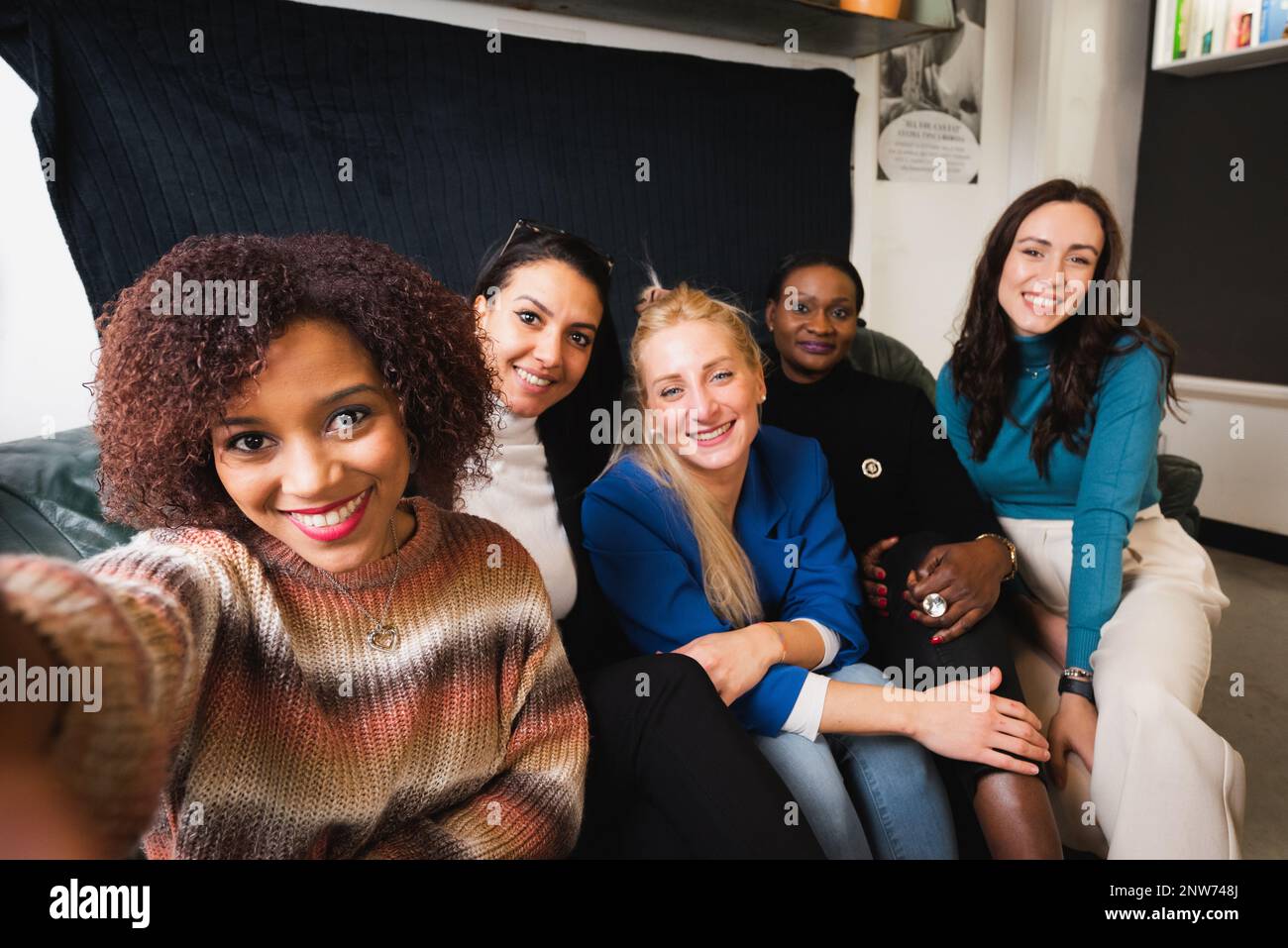 Eine Gruppe legerer Frauen mit unterschiedlicher ethnischer Zugehörigkeit macht Selfie auf dem Sofa. Stockfoto