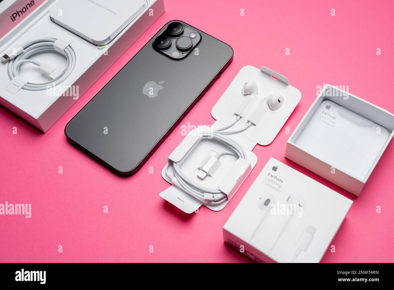 Neues iPhone 14 pro max und Apple Ohrhörer, AirPods weiße Ohrhörer zum Anhören von Musik und Podcasts in einer offenen Verpackung. Isolierter rosafarbener Hintergrund. Budapes Stockfoto