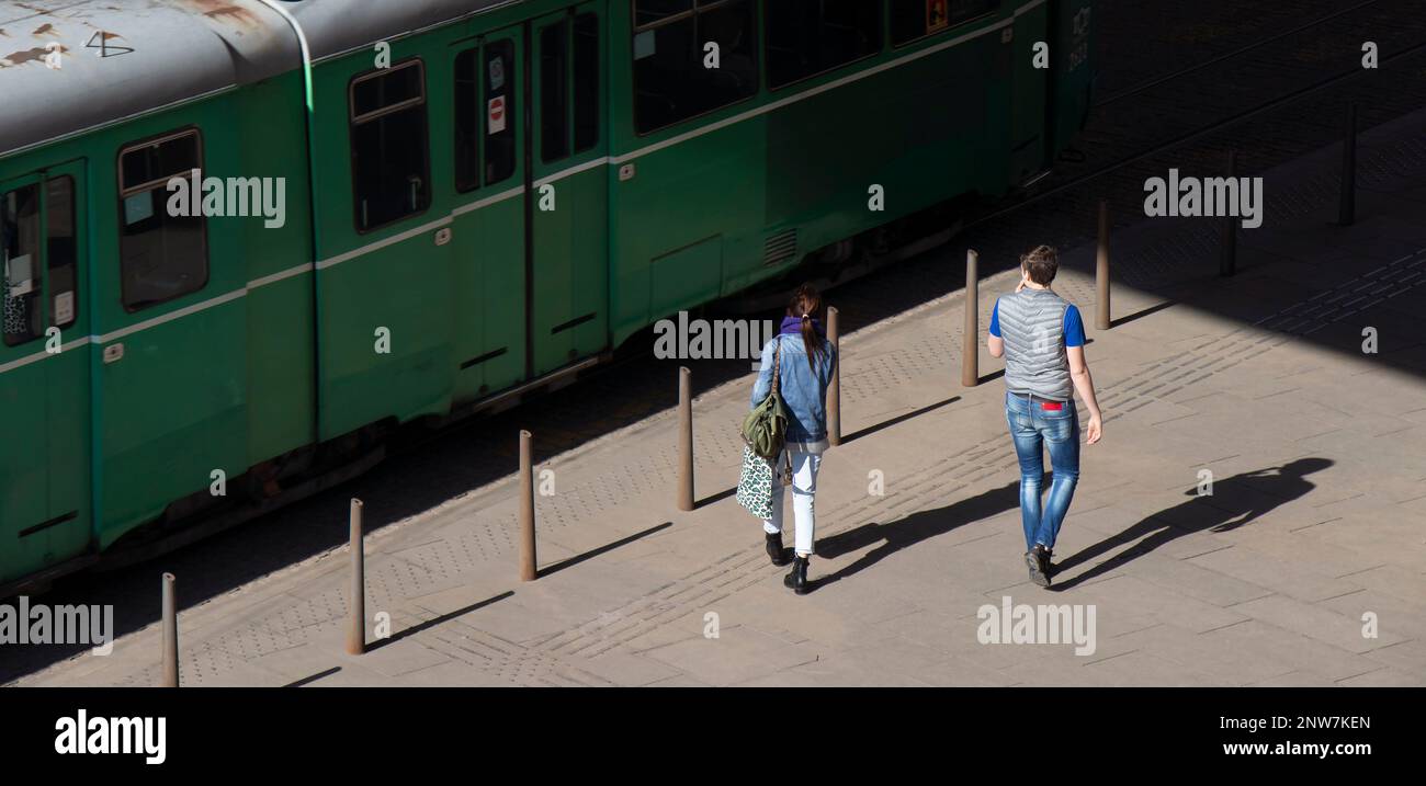 Belgrad, Serbien - 23. Februar 2023: Zwei junge Menschen nähern sich der grünen Straßenbahn an der Haltestelle für öffentliche Verkehrsmittel, hohe Rückansicht Stockfoto