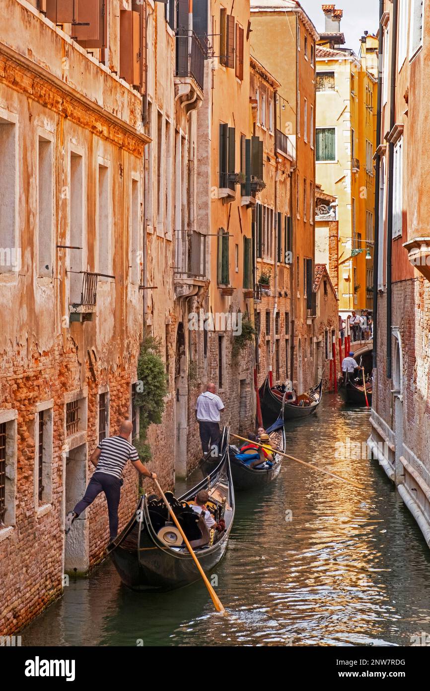 Gondoliere in traditionellen Gondeln nehmen Touristen mit auf Besichtigungstouren entlang der engen Kanäle in Venedig, Venetien, Nordostitalien Stockfoto