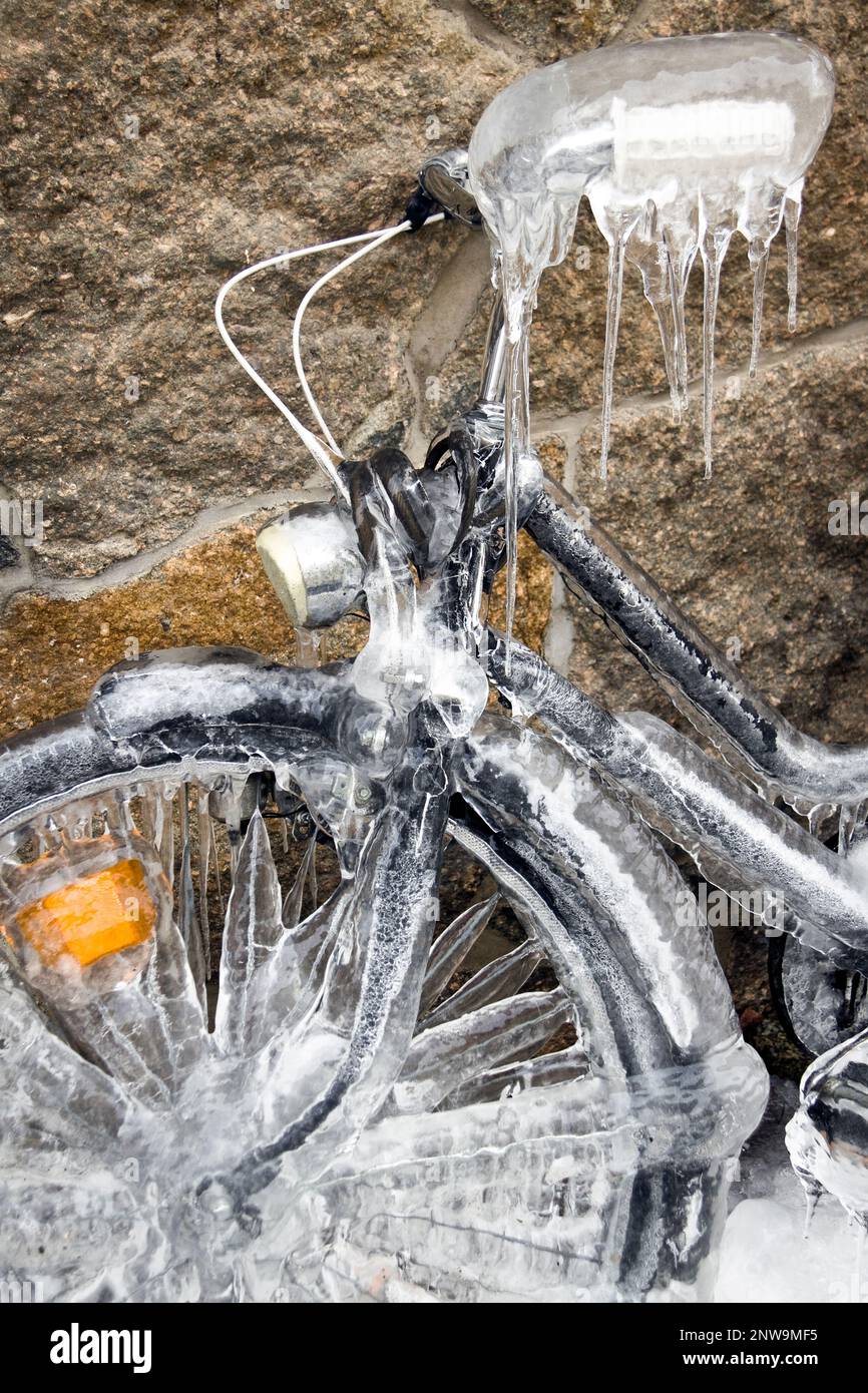 Vertikale Nahaufnahme eines gefrorenen, eisbedeckten Fahrrads, das sich gegen eine Steinwand neigt. Ein Fahrrad bedeckt mit Eis, eiskalte Temperaturen im kalten Winter Stockfoto