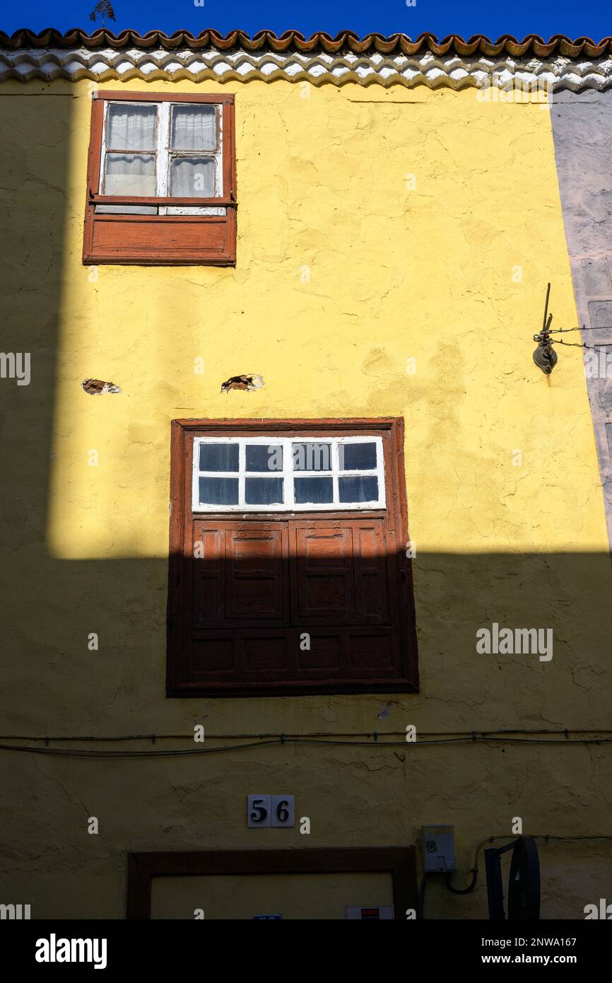 Die helle Wintersonne unterstreicht die lebendige gelbe Wand und die traditionellen kanarischen Fenster in einem Gebäude in La Laguna, Teneriffa. Stockfoto