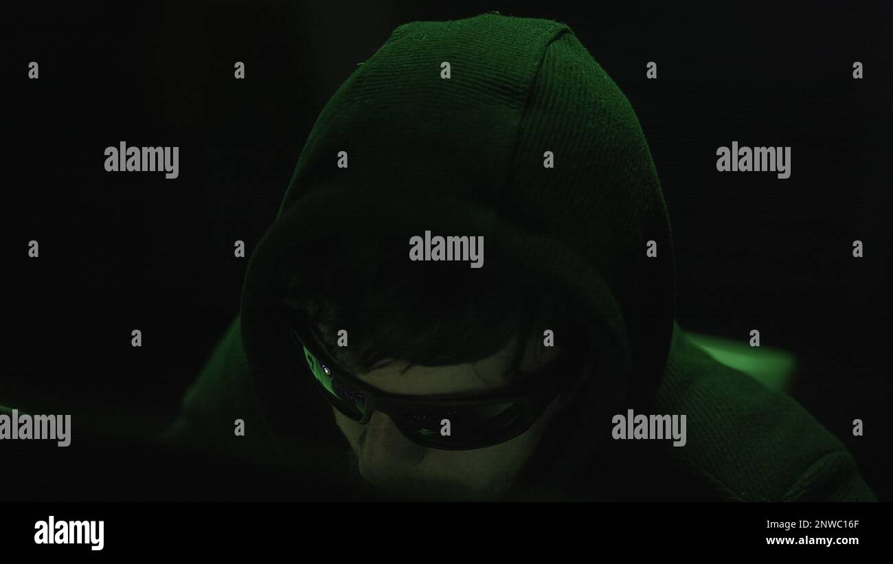 Cyberkriminelles Hacken in einem dunklen Raum mit geheimnisvollen grünen Lichtern, Nahaufnahme Stockfoto