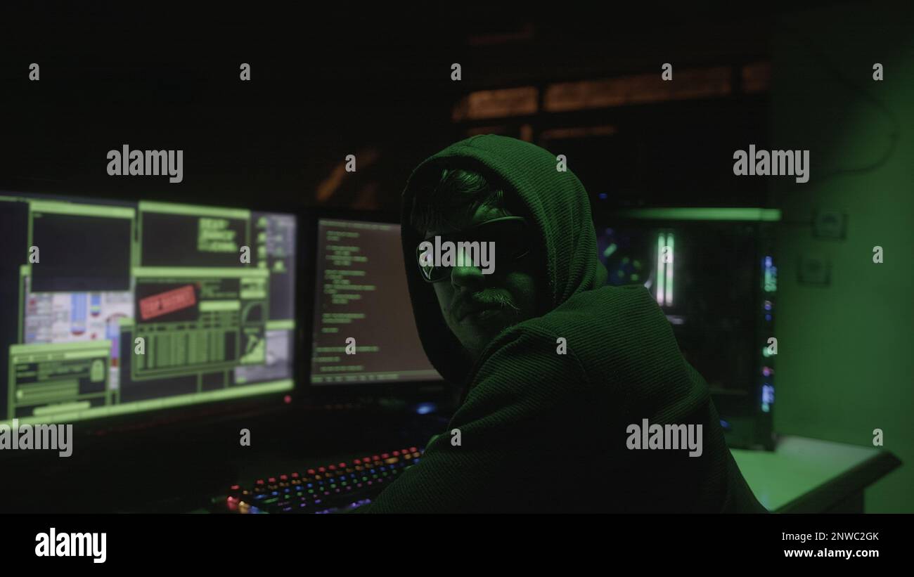 Schwarzer, brillanter junger Hacker mit Kapuze und zwei Monitoren beim Hacken und Betrachten der Kamera, Nahaufnahme Stockfoto