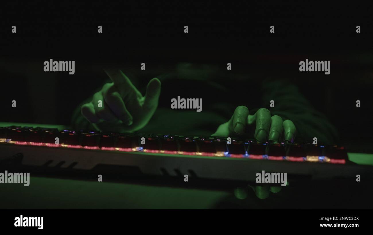 Farbige RGB-Tastatur, die Hacker oder Coder schreibt Code mit den Fingern auf grünes Licht Stockfoto