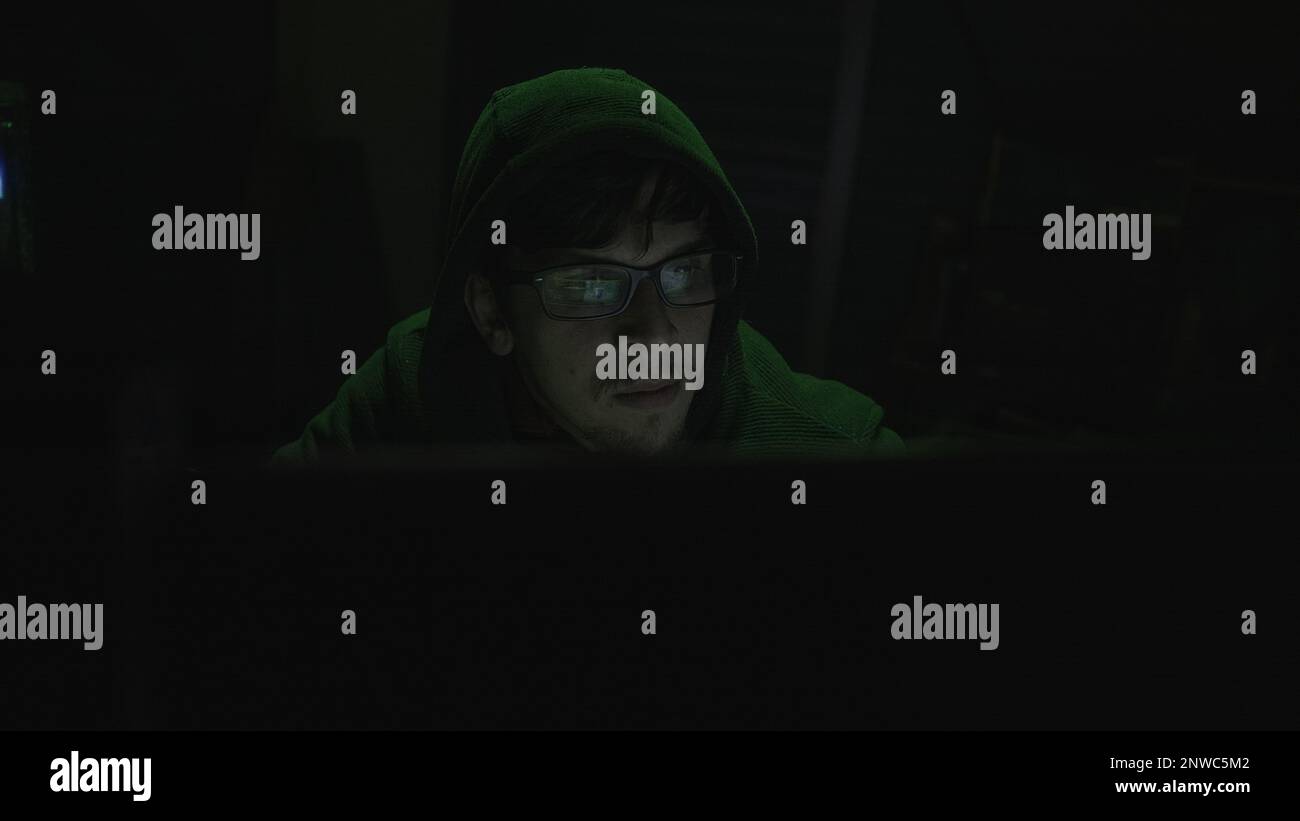 World of Hacking, junger Programmierer mit Hoodie und schwarzen Brillen, die in Codierung mit grüner Beleuchtung eintauchen Stockfoto