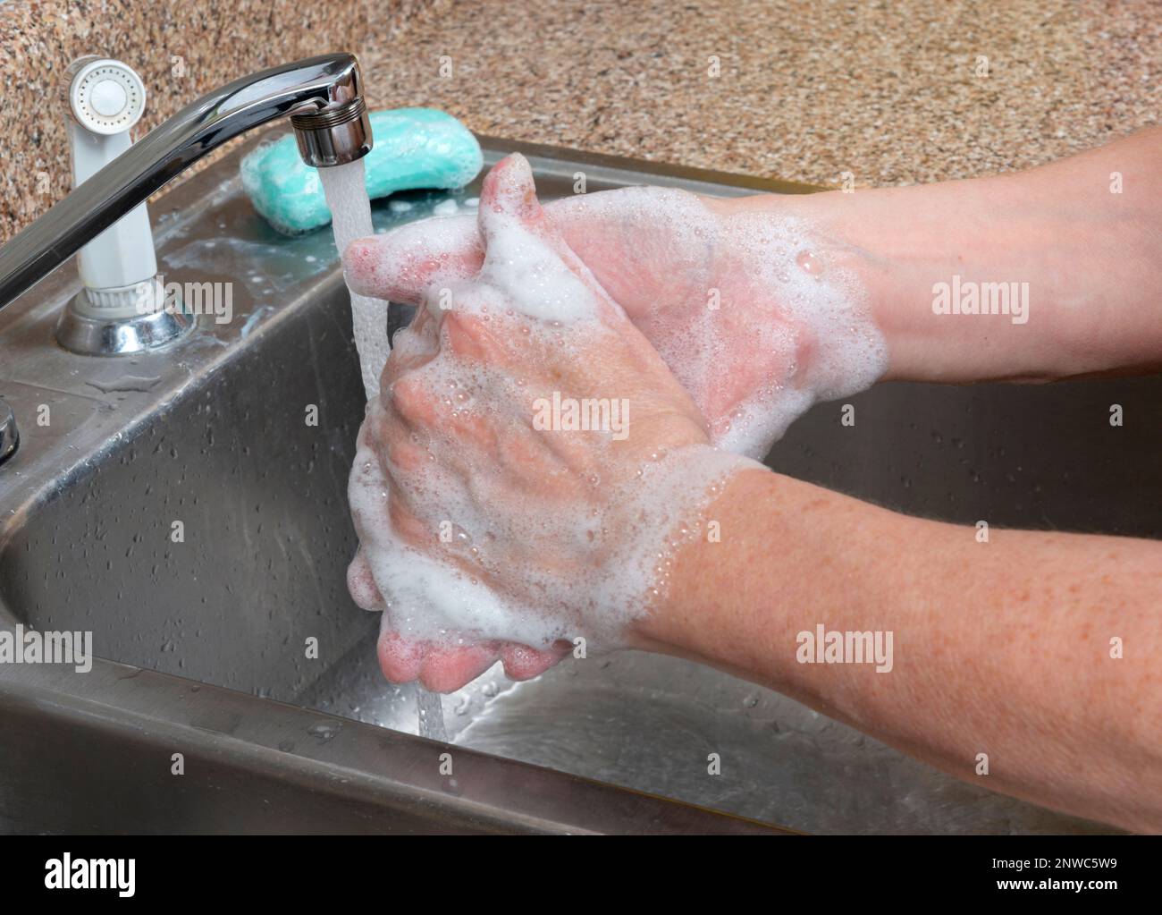 Horizontale Aufnahme einer Frau, die ihre Hände im Spülbecken wäscht, mit fließendem Wasser und einem Stück Seife auf dem Spülbrett. Stockfoto