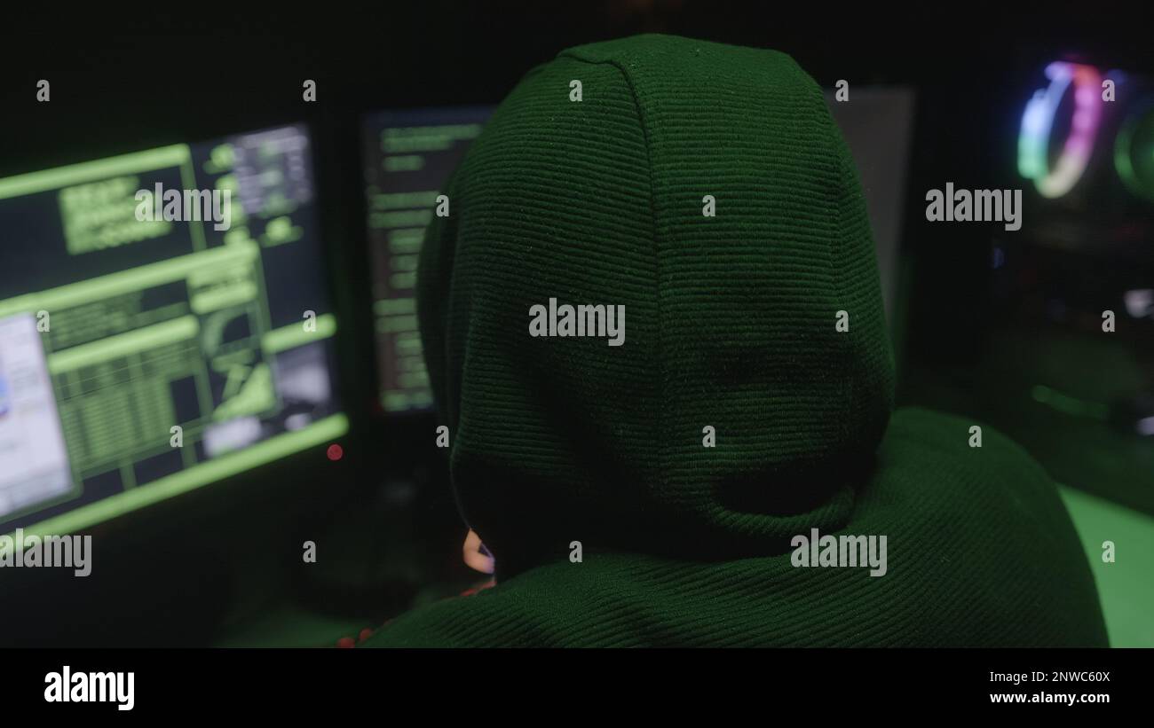 Junger männlicher Hacker oder Programmierer in Kapuzenpulli, der sich mit dem Rücken zum Computer hackt Stockfoto