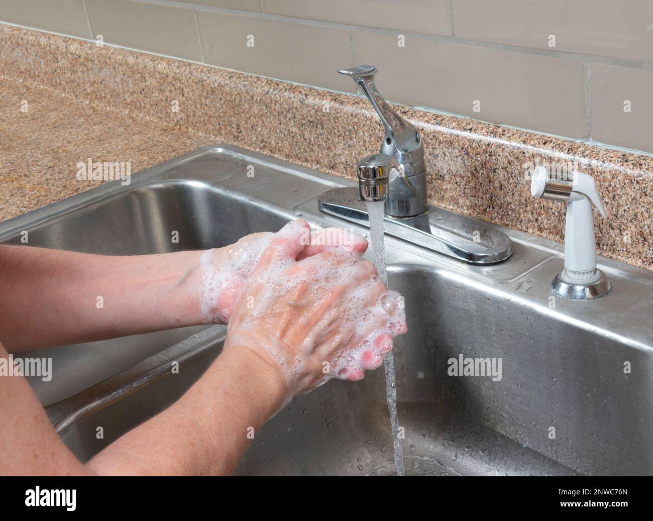 Horizontale Aufnahme einer älteren Frau, die ihre Hände im Spülbecken wäscht, mit fließendem Wasser. Stockfoto