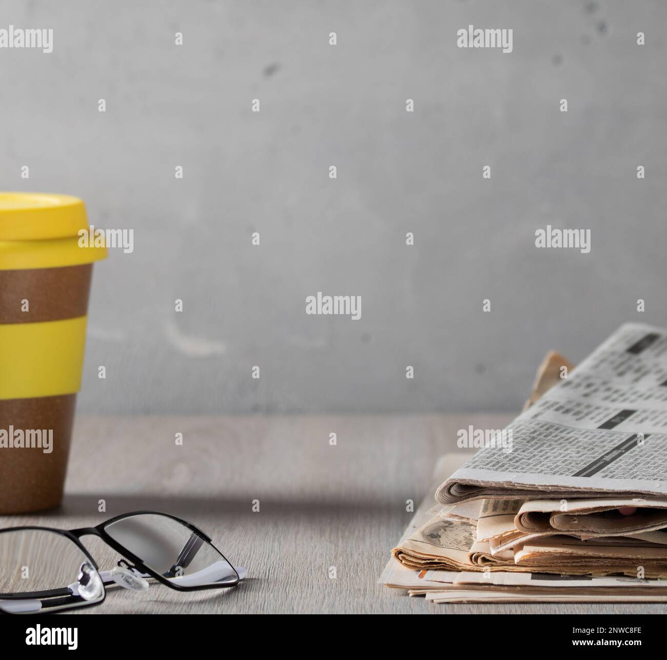 Morgen, bevor wir zur Arbeit gehen. Gemütliche Heimszene - ein Stapel alter Zeitungen, Gläser und ein Glas Kaffee auf einem Holztisch Stockfoto