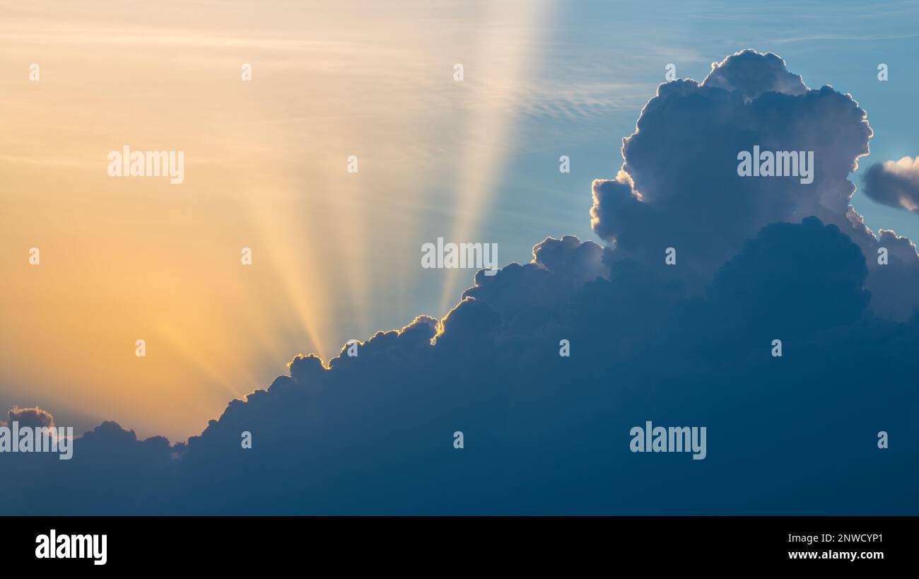 Dramatischer Sonnenuntergang mit langen Sonnenstrahlen in der sommerlichen Wolkenlandschaft in der malerischen Abenddämmerung. Wunderschöner Kontrast zwischen gelben Sonnenstrahlen und dunkelblauer Wolke am Himmel. Stockfoto