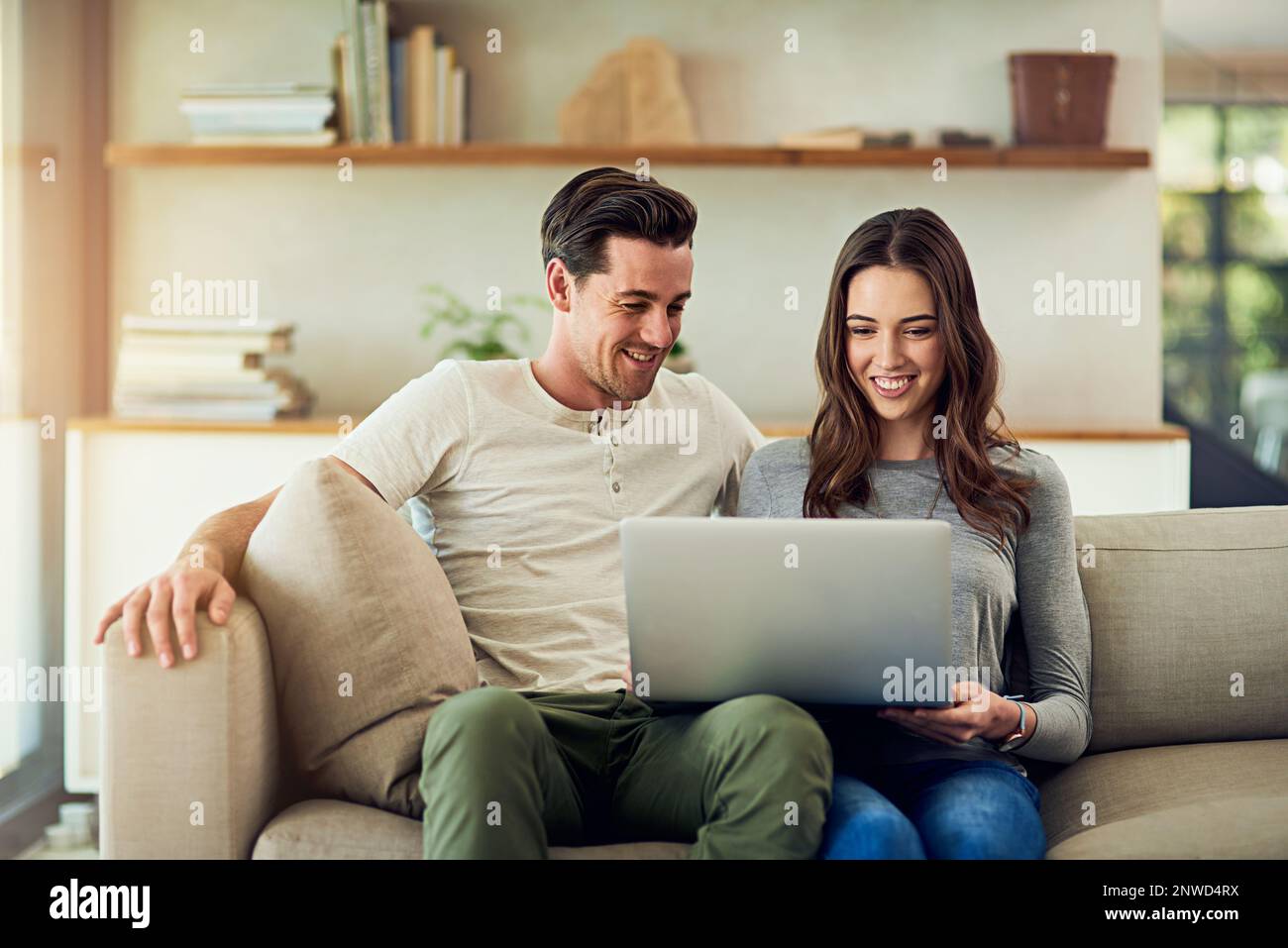 Das Online-Erlebnis ist noch besser, wenn es geteilt wird. Aufnahme eines glücklichen jungen Paares, das zu Hause einen Laptop auf dem Sofa benutzt. Stockfoto