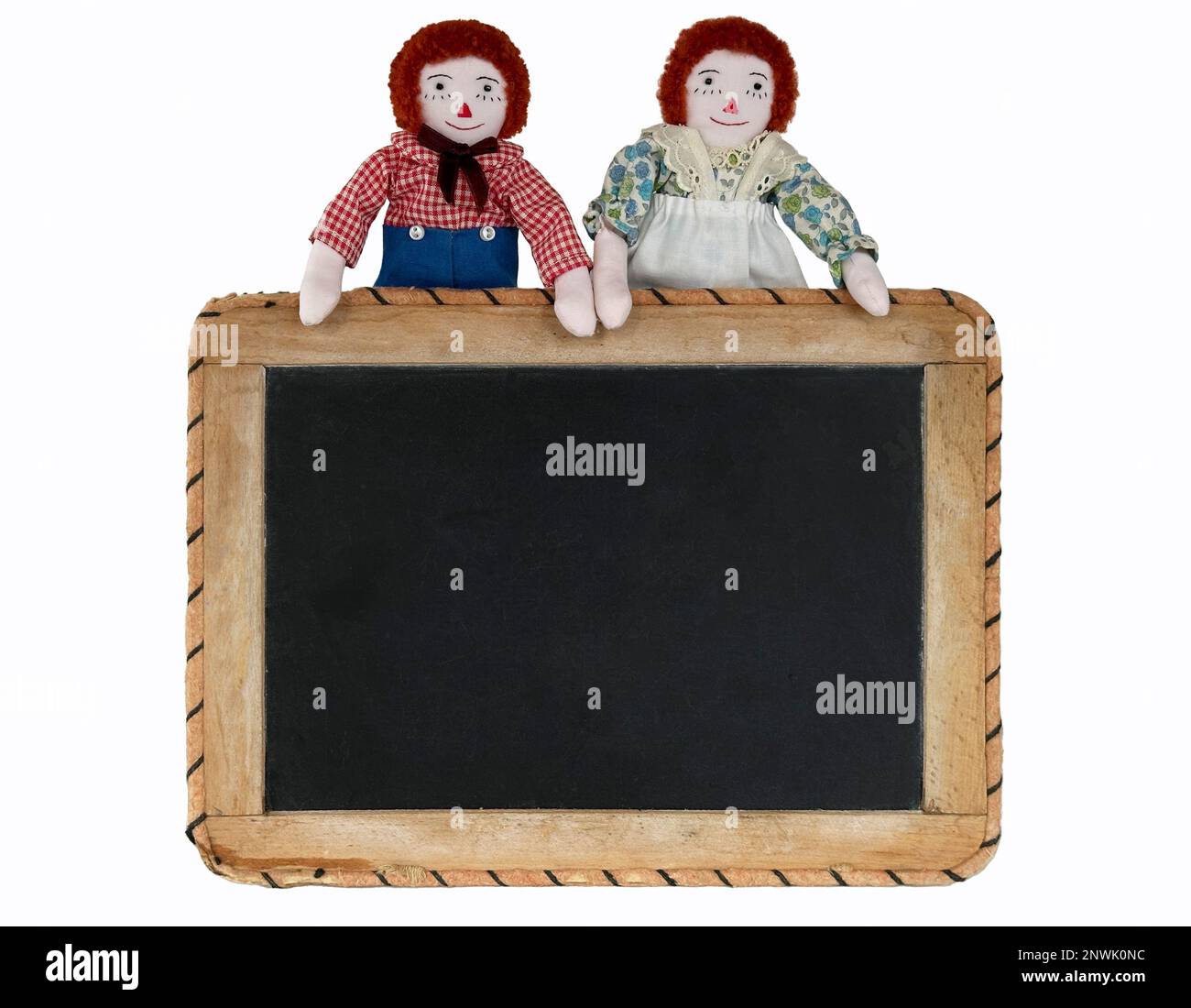 Raggedy Ann & Raggedy Andy halten ein Schild für Ihre Nachricht, Nachricht, Ankündigung. Isolierter Ausschnitt für Sie. Mini-Stoffpuppen halten sich am Spielbrett fest. Stockfoto