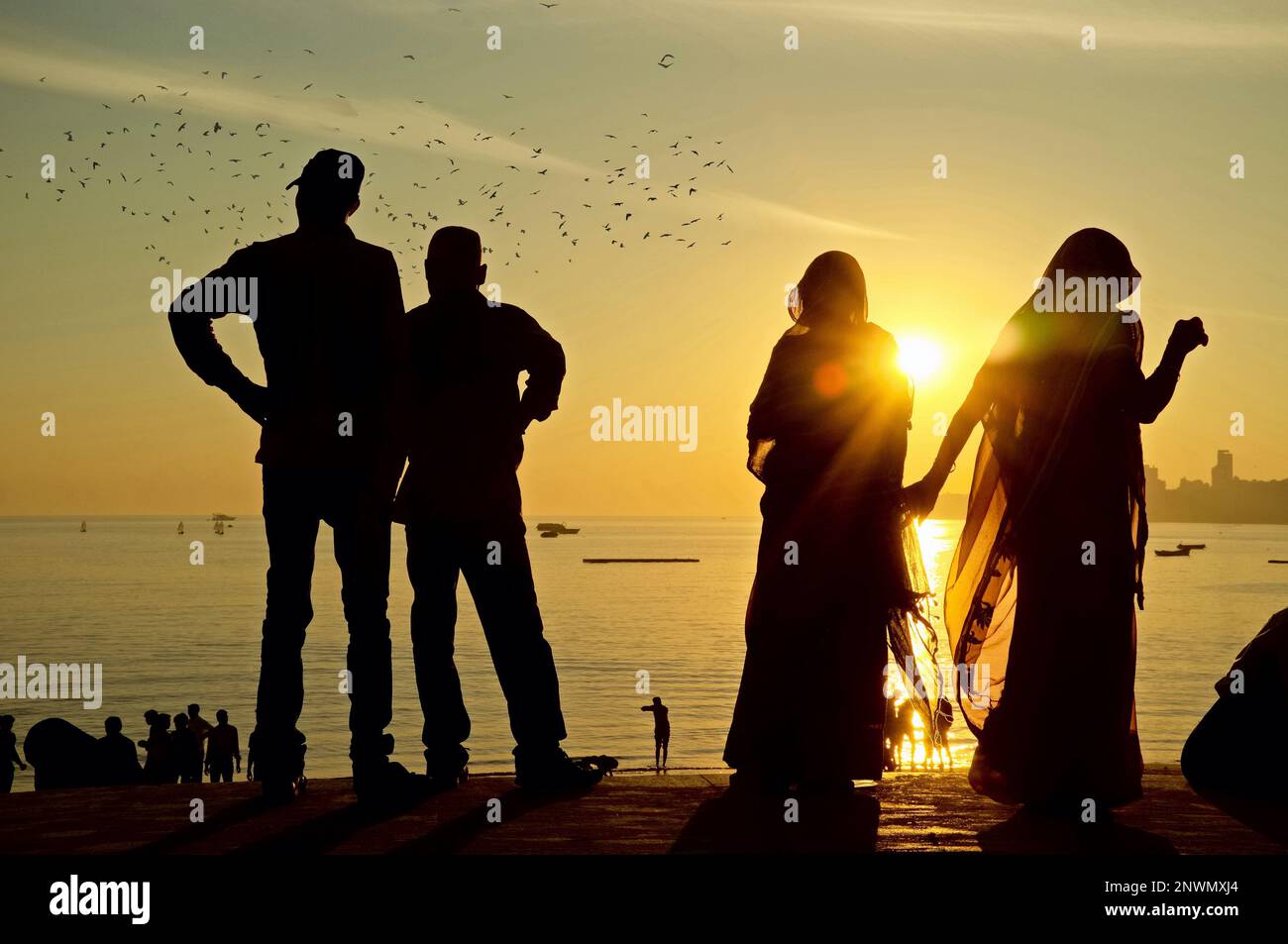 Sonnenuntergang am Marine Drive, Mumbai, Maharashtra, Indien, zwei indische Paare, die an der Ufermauer stehen und als Silhouetten erscheinen Stockfoto