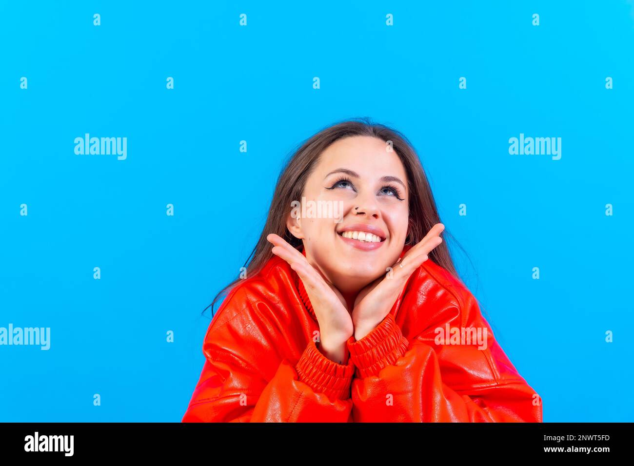 Nahaufnahme einer jungen Frau, fröhlich oder lachend, isoliert auf blauem Studiohintergrund in roter Windjacke Stockfoto
