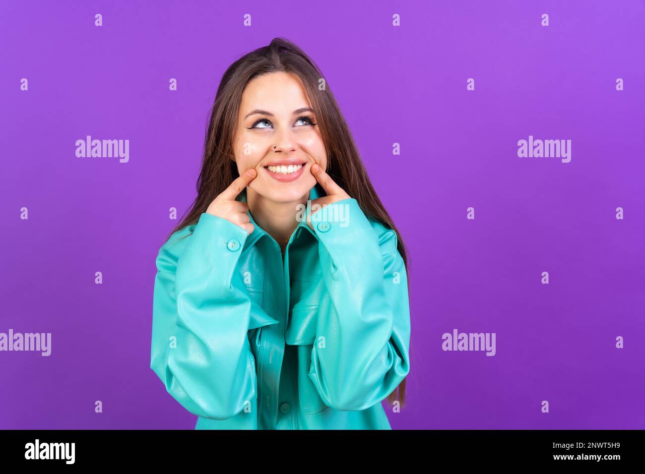 Nahaufnahme von einer jungen Frau, fröhlich isoliert auf lila Studiohintergrund in blauer Windjacke Stockfoto