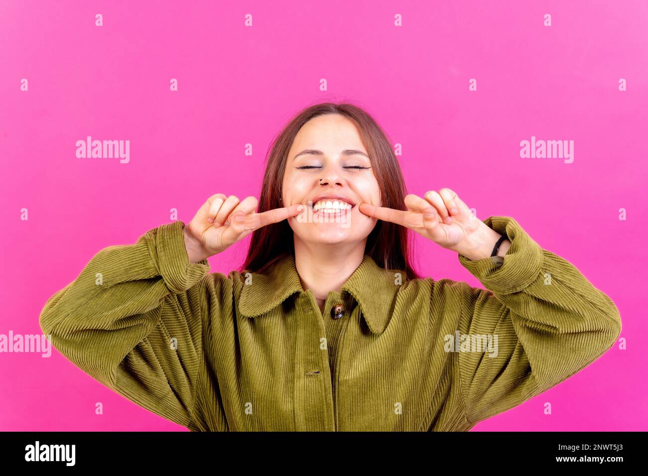 Nahaufnahme von einer jungen Frau, fröhlich oder lachend, isoliert auf pinkfarbenem Studiohintergrund in grüner Windjacke Stockfoto