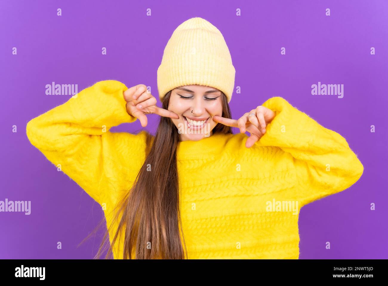 Nahaufnahme einer jungen, fröhlichen Frau, isoliert auf lila Studiohintergrund in gelbem Wollpullover, der lächelt Stockfoto
