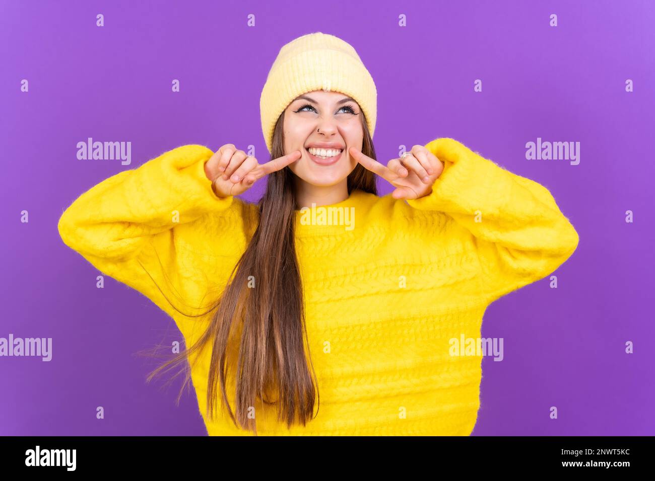 Nahaufnahme einer jungen, fröhlichen Frau, isoliert auf lila Studiohintergrund in gelbem Wollpullover, der lächelt Stockfoto
