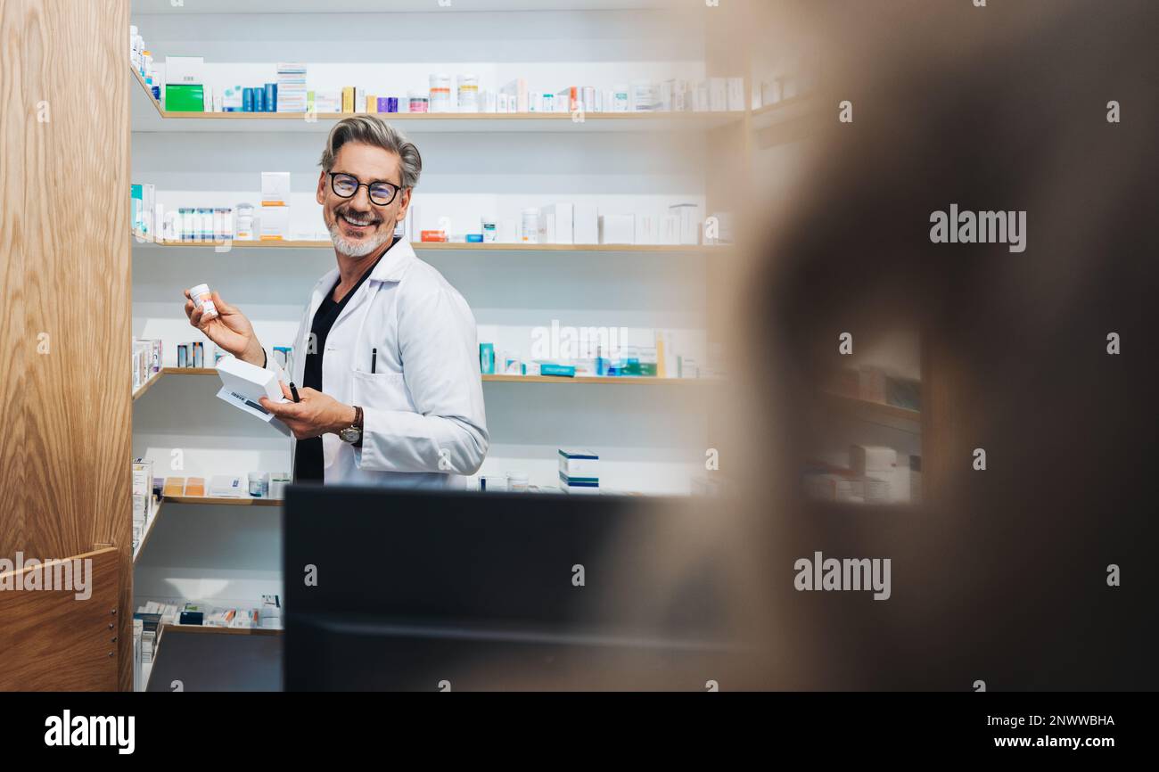 Apotheker, der verschreibungspflichtige Medikamente aus einem Regal in einer Apotheke holt. Seniorenmediziner, der einem Patienten in einer Apotheke assistiert. Stockfoto