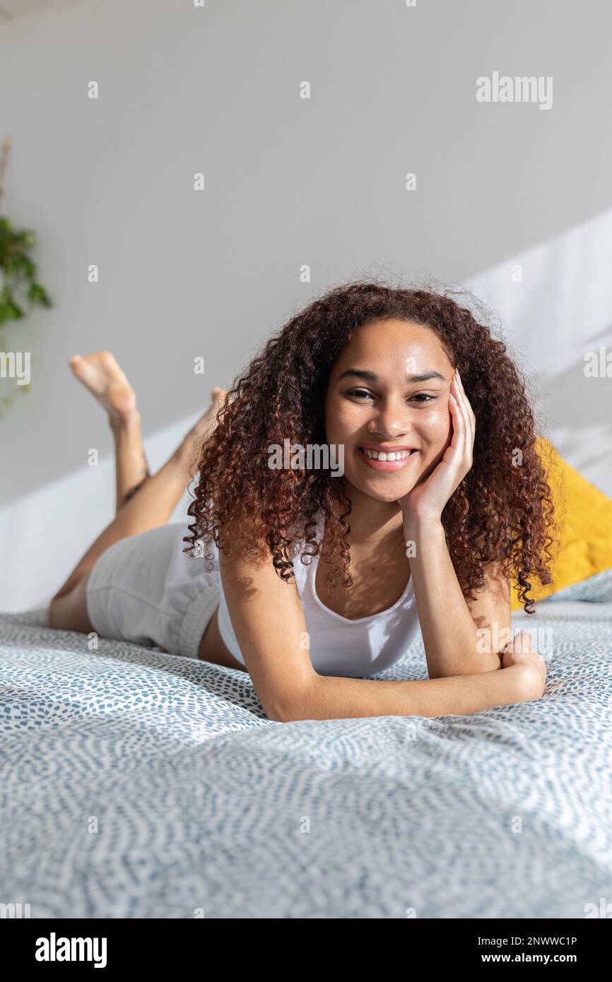 Porträt einer lächelnden jungen lateinamerikanischen Frau, die morgens im Bett entspannt Stockfoto