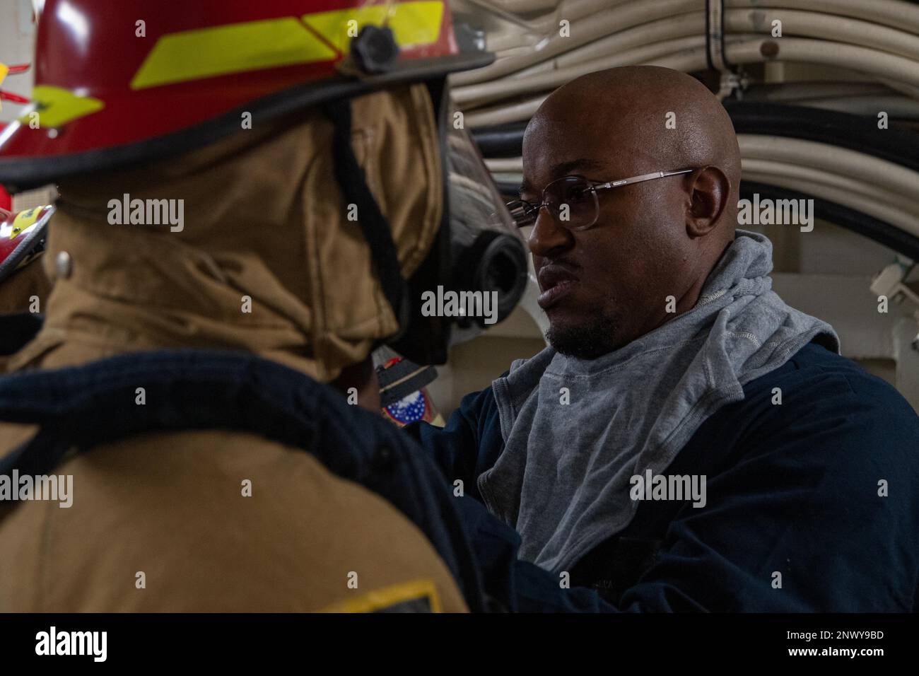 PHILIPPINE SEA (28. Januar 2023) Damage Controlman 2. Class Joshua Meyers, Right, aus Detroit, zugewiesen an den nach vorn eingesetzten amphibischen Angriffsträger USS America (LHA 6) assistiert Machinist's Mate 2. Class Cipriano Garcia, Left, aus San Antonio, ebenfalls nach Amerika, und legt während einer Übung Feuerwehrausrüstung an; Während der Fahrt in der Philippinischen See am 28. Januar. America, das führende Schiff der America Amphibious Ready Group, ist im 7.-Flottenbereich tätig. 7. Fleet sind die USA Die größte Flotte der Navy, die in erster Linie eingesetzt wird, ist nummeriert und interagiert routinemäßig Stockfoto