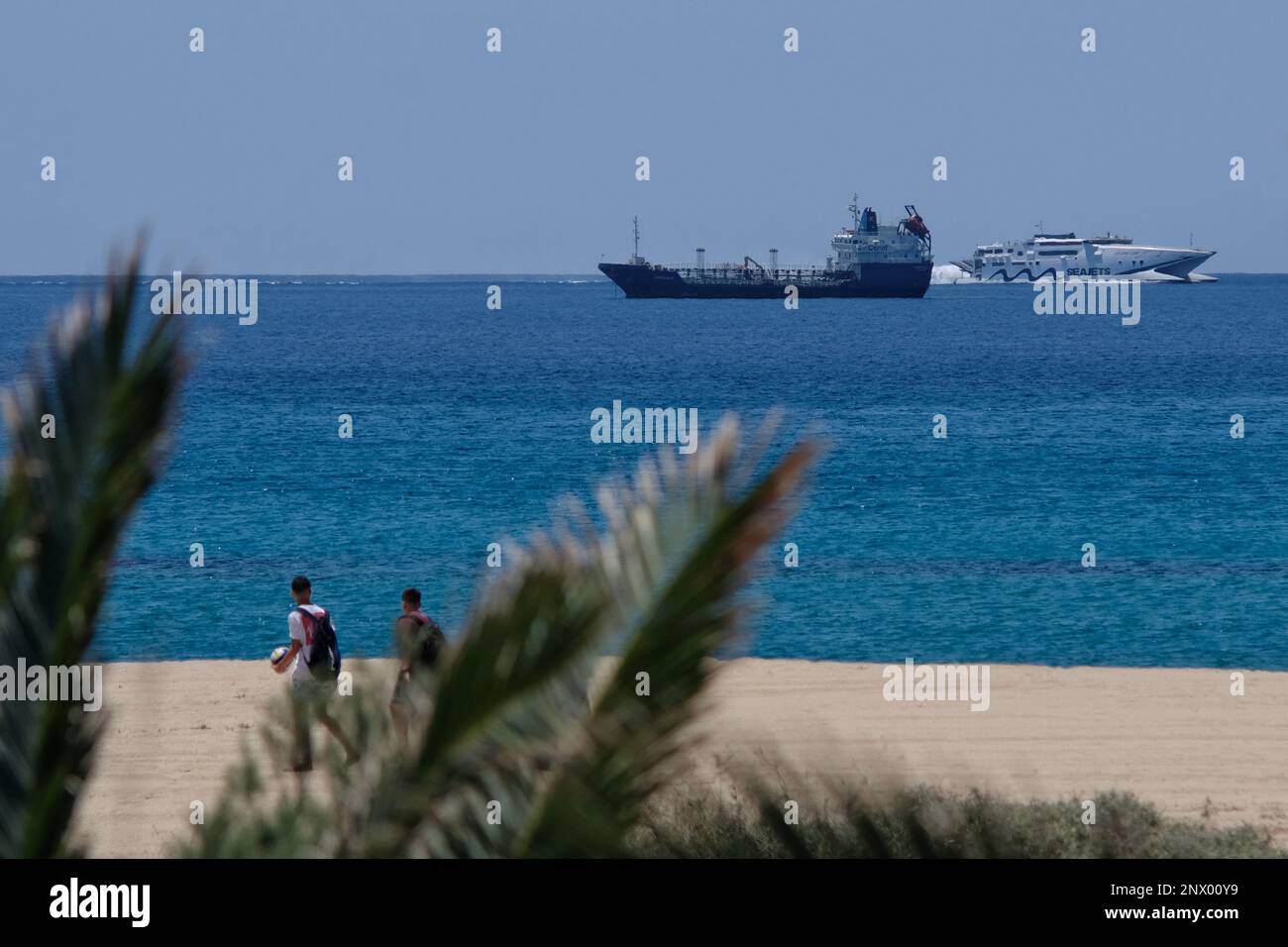 IOS, Griechenland : 29. Mai 2021 : Blick auf Touristen, die am Mylopotas-Strand in iOS Griechenland spazieren, ein Frachtschiff und ein Hochgeschwindigkeitsboot im Hintergrund Stockfoto