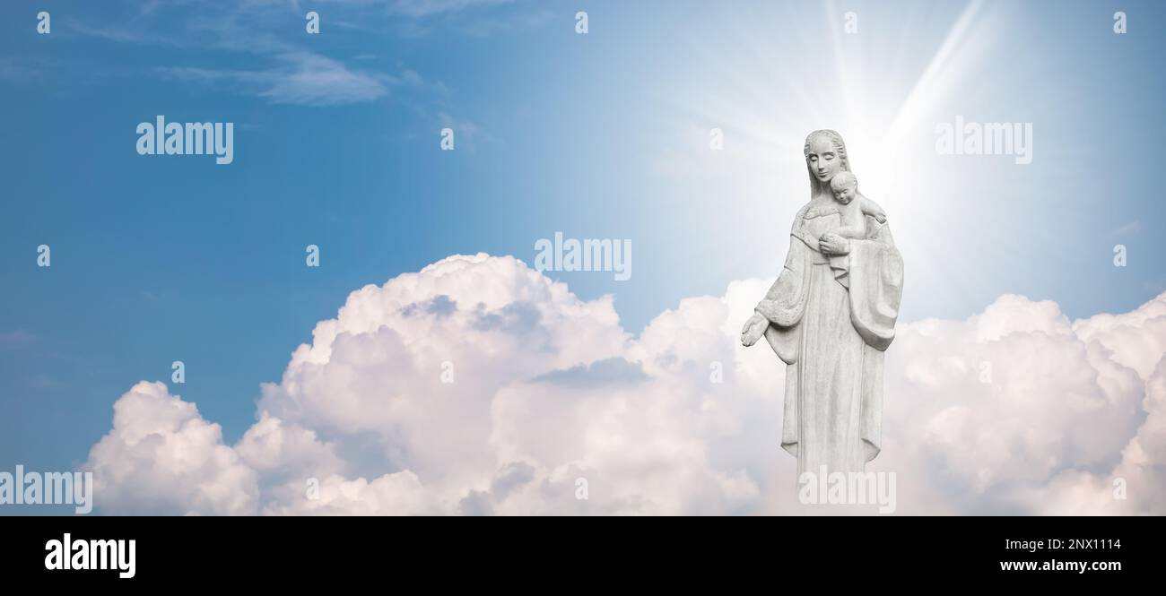 Statue von Mutter Maria und Baby Jesus vor blauem Himmel mit weißen Wolken im Hintergrund. Stockfoto