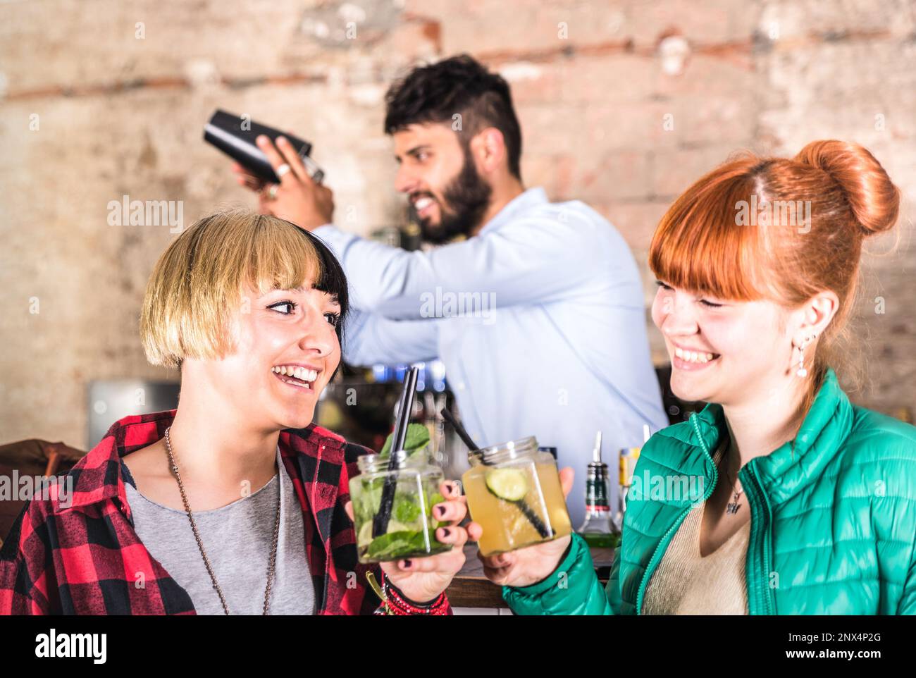 Ein paar Freundinnen, die sich in der Mode-Cocktailbar amüsieren - professioneller Barkeeper, der sich hinter jungen betrunkenen Frauen ausschüttet - Nachtleben-Konzept bei Party Night Stockfoto