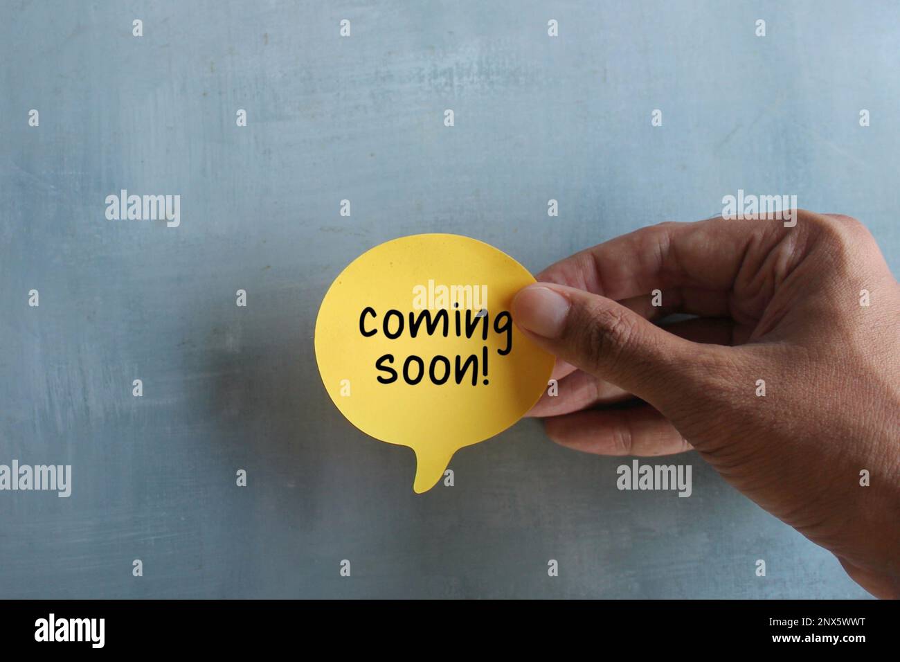 Handgehaltene Sprechblase mit Text, DER IN KÜRZE auf Betonwand ERSCHEINT. Stockfoto