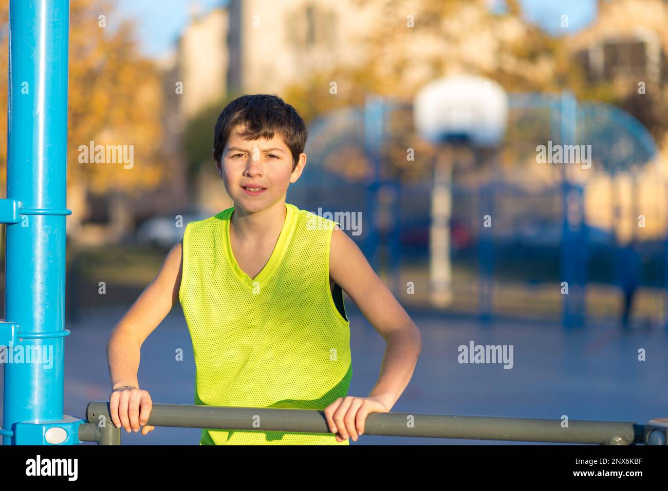 Porträt eines lächelnden Jungen in einem Tanktop, der in der Dämmerung auf einem städtischen Basketballfeld in die Kamera lächelt. Stockfoto