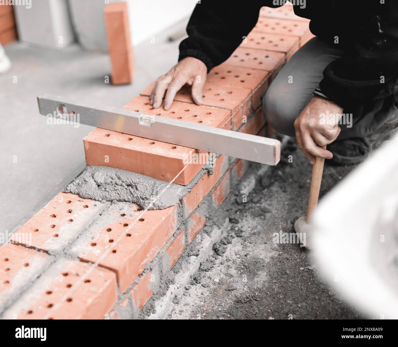 Handwerker, der die Höhe der Ziegelwand mit der Wasserwaage überprüft Stockfoto