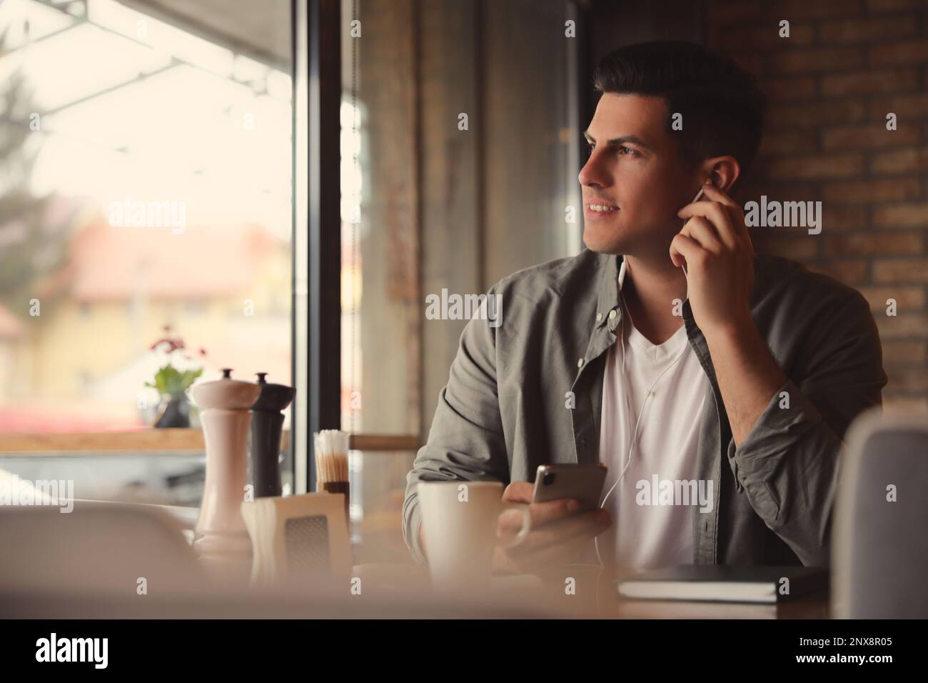 Mann mit Smartphone, der Hörbuch am Tisch im Café hört Stockfoto