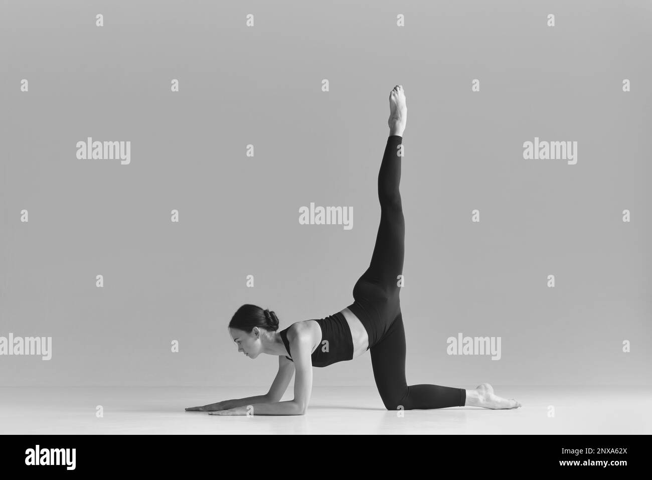 Flexibilität. Schwarzweißfotografie. Ein junges Mädchen, das Stretching macht, das Bein hochhebt, im Studio trainiert. Sportbegriff Stockfoto