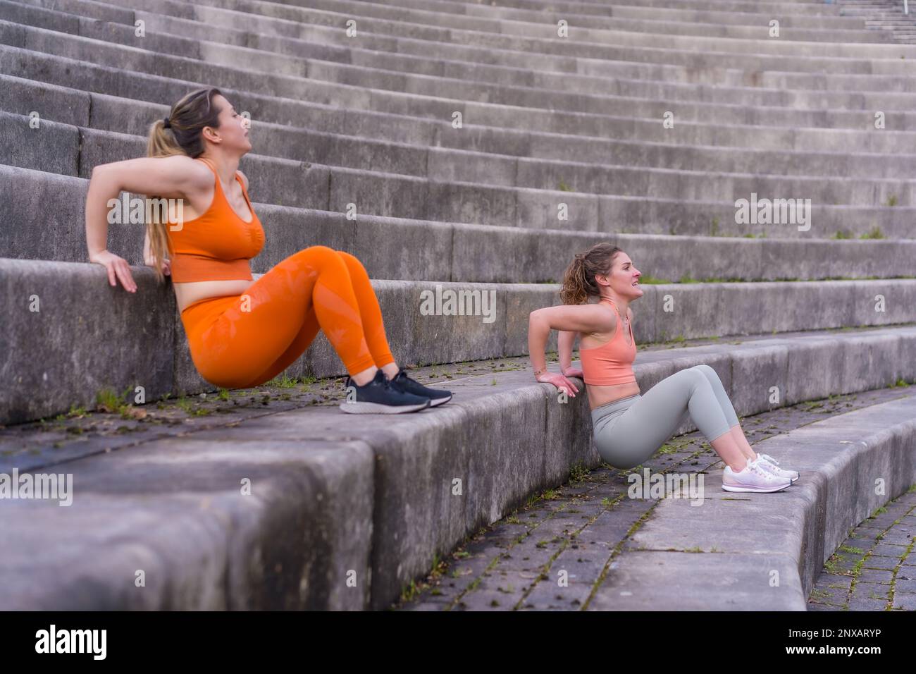Zwei junge, weiße Sportlerinnen, die Tricep-Dips auf einer Treppe machen Stockfoto