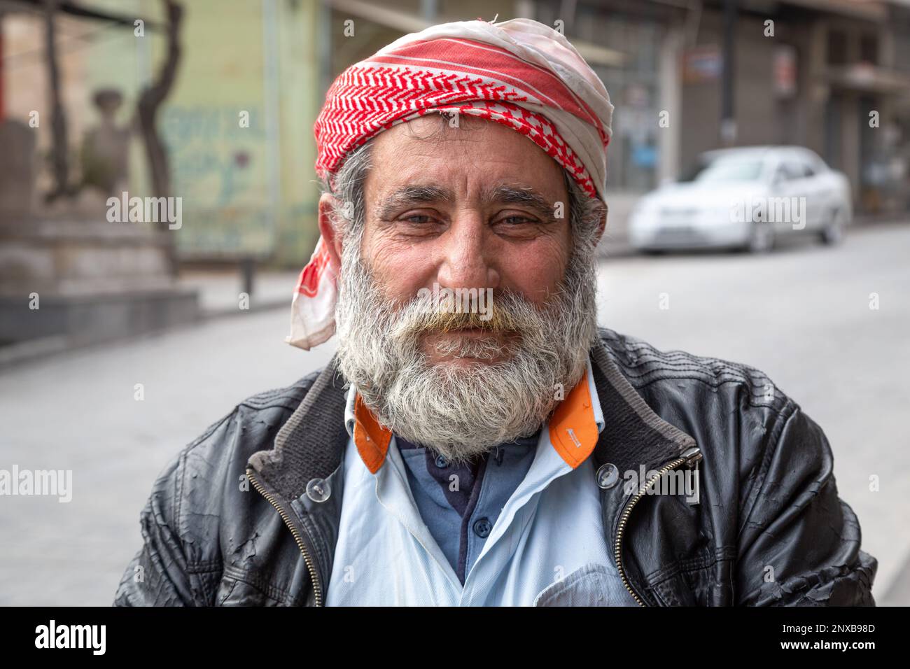 Porträtfoto eines lächelnden Syrern. Porträt eines Syrers mit einem traditionellen Schleier aus „Pushi“ und einem durch Zigarettenrauch vergilbten Schnurrbart. Stockfoto