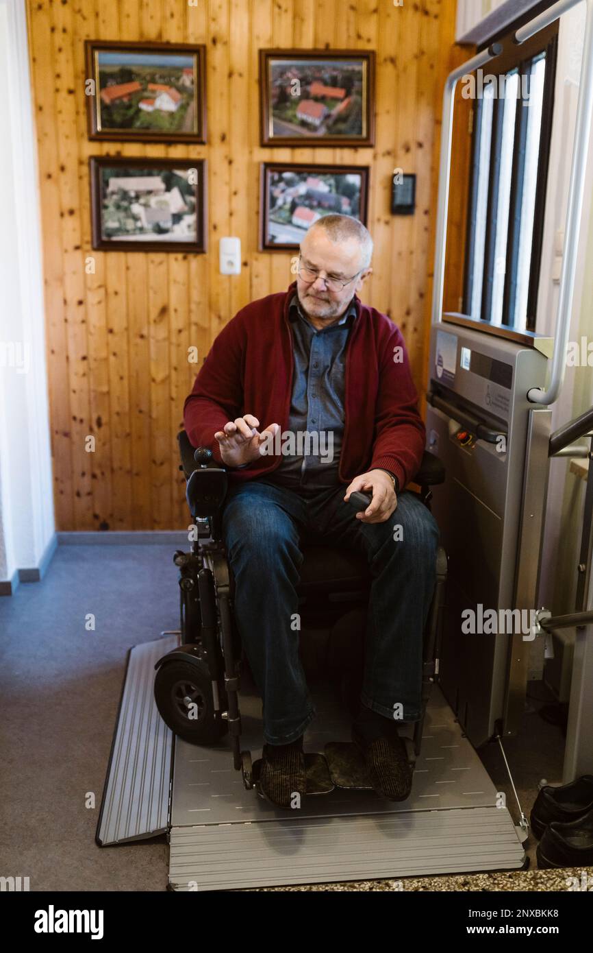 Die volle Länge eines pensionierten Seniorenmannes mit Behinderung im motorisierten Rollstuhl zu Hause Stockfoto