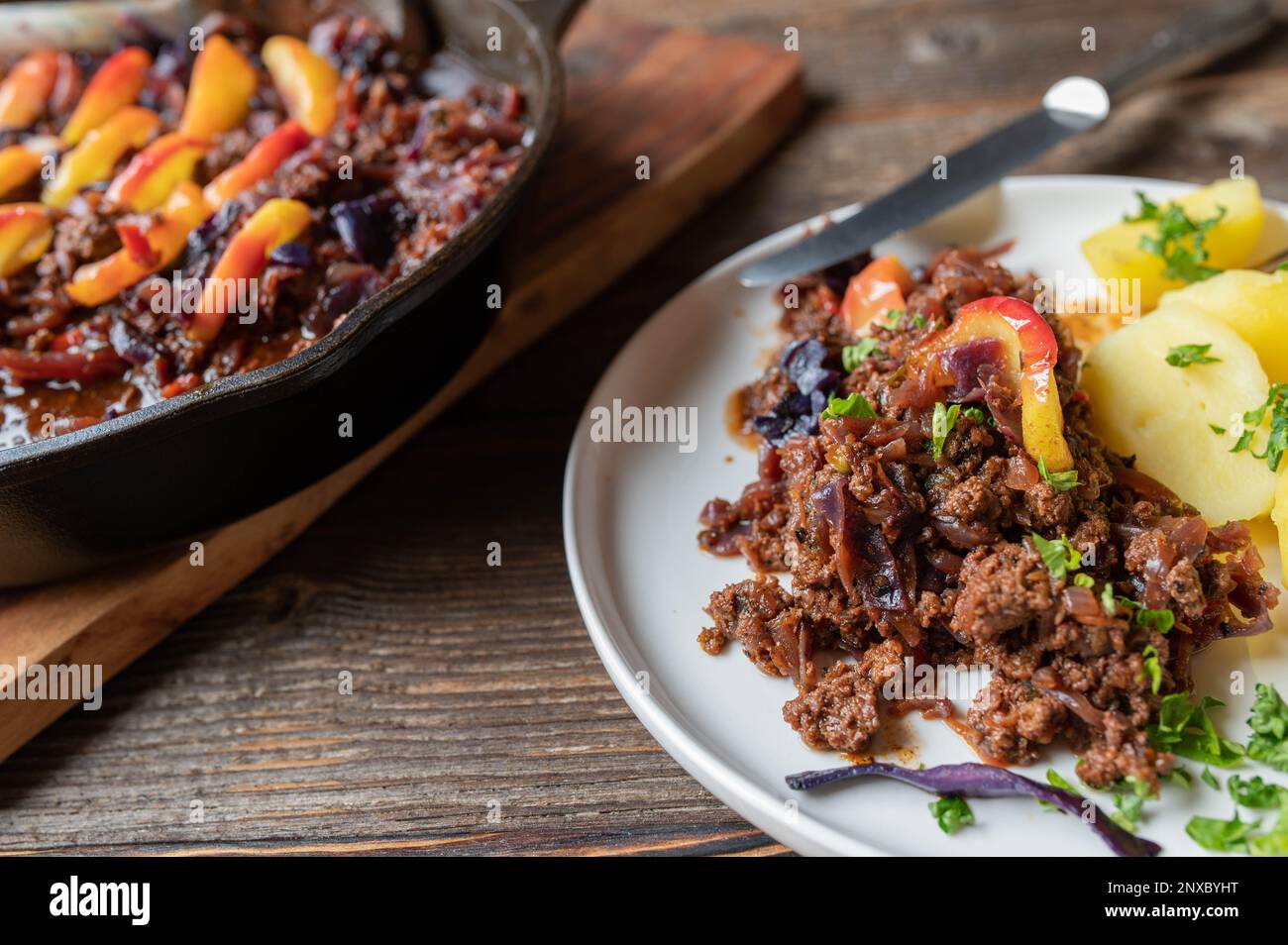 Rindereintopf mit Rotkohl und gekochten Äpfeln und Kartoffeln auf einem Holztisch Stockfoto