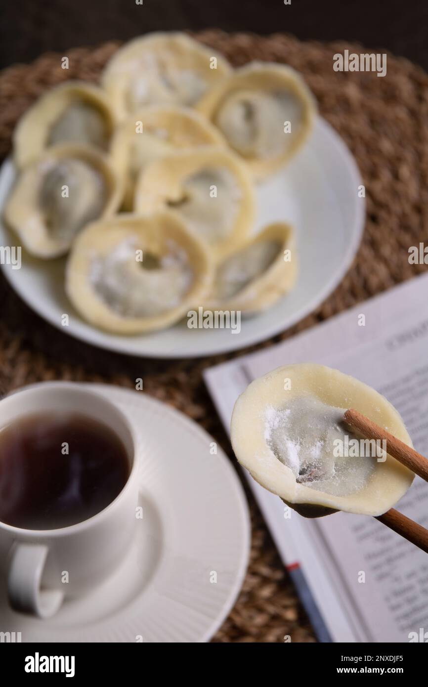 Machen Sie Fotos von vielen Schokoladensüßen in Form von Knödeln, die auf einem Teller neben einem Buch und einer Kaffeetasse mit einem Getränk auf einem Korbstand liegen Stockfoto