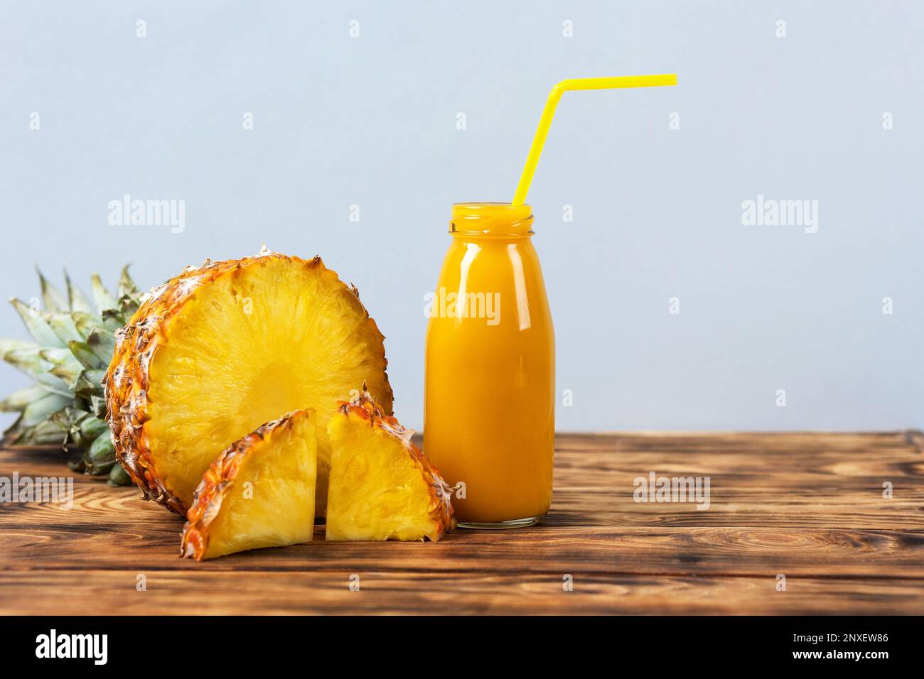 Scheiben saftiger Ananas und ein frischer, gesunder Smoothie in einer Glasflasche und einem Strohhalm auf einem Holzbrett auf Holzhintergrund. Gesund, Entgiftung Stockfoto
