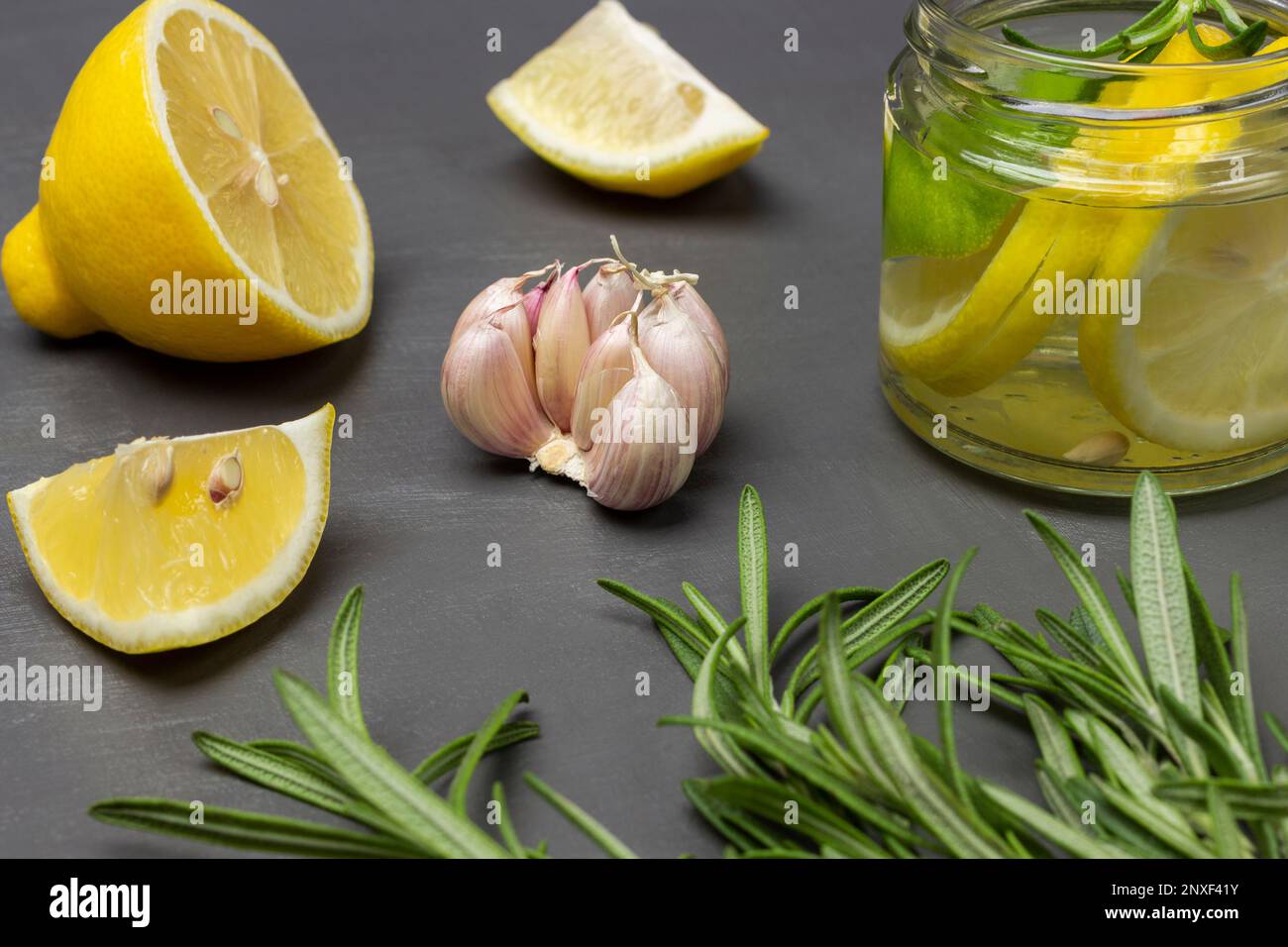 Rosmarinzweige, Knoblauch und Zitrone auf dem Tisch. Zitronengetränk in einem Glasgefäß. Schließen. Grauer Hintergrund. Stockfoto