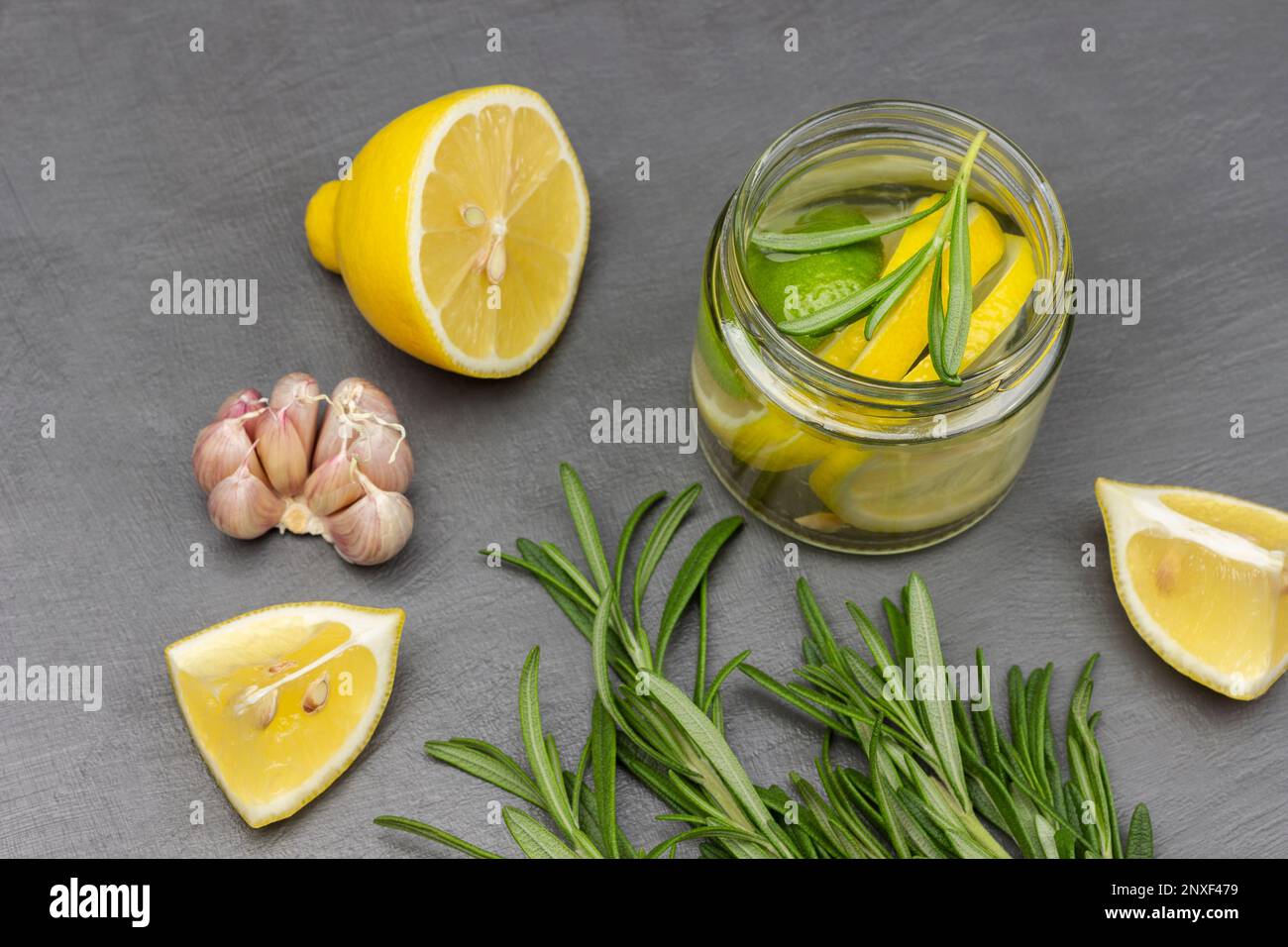 Knoblauch, Rosmarin-Zweige und Zitrone auf dem Tisch. Zitronengetränk in einem Glasgefäß. Flach verlegt. Grauer Hintergrund. Stockfoto