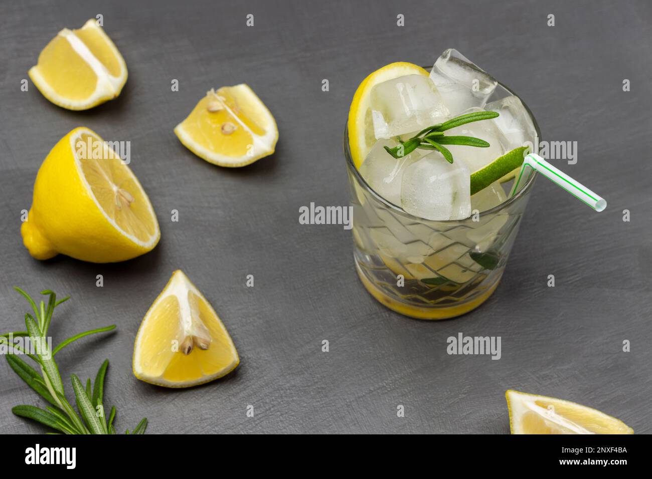 Ein Glas Sommergetränk mit Eis und Zitrone. Zitronenscheiben auf dem Tisch. Flach verlegt. Grauer Hintergrund. Stockfoto