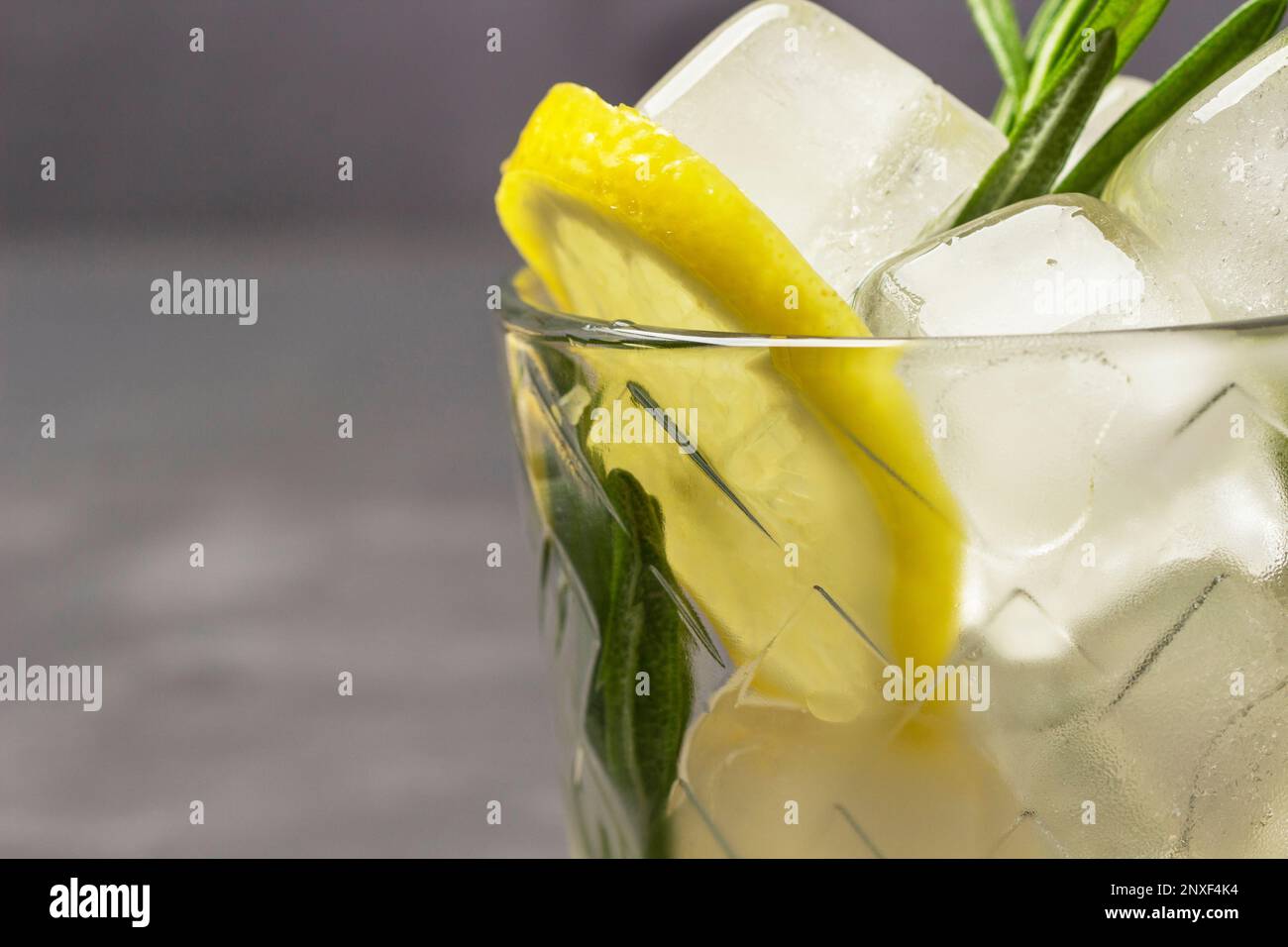 Zitrone und Eisstücke in einem Glas. Teil des Rahmens. Speicherplatz kopieren. Schließen. Grauer Hintergrund. Stockfoto