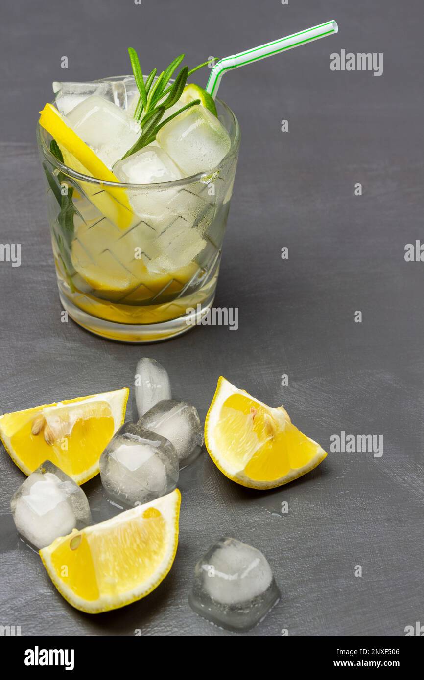 Sommerliches Kühlgetränk mit Zitrone und Eis, Strohhalm in einem Glas. Zitronen und Eis auf dem Tisch. Draufsicht. Grauer Hintergrund. Stockfoto