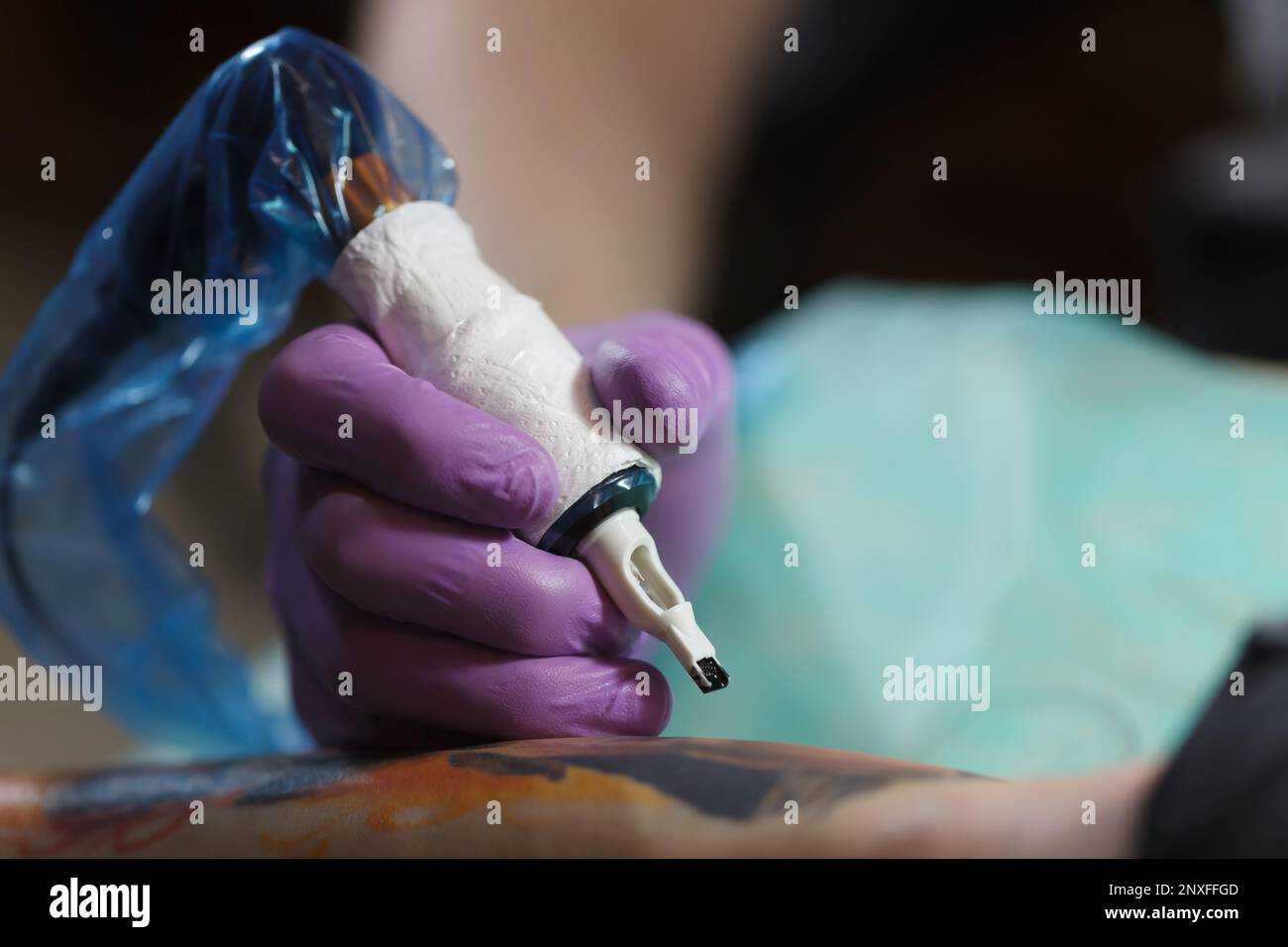 Tattoo-Meister, der mit der Drehmaschine arbeitet. Professioneller Tätowierer trägt sterile Handschuhe und verwendet eine moderne Pistole, um Tintenkunst auf der Haut zu kreieren Stockfoto